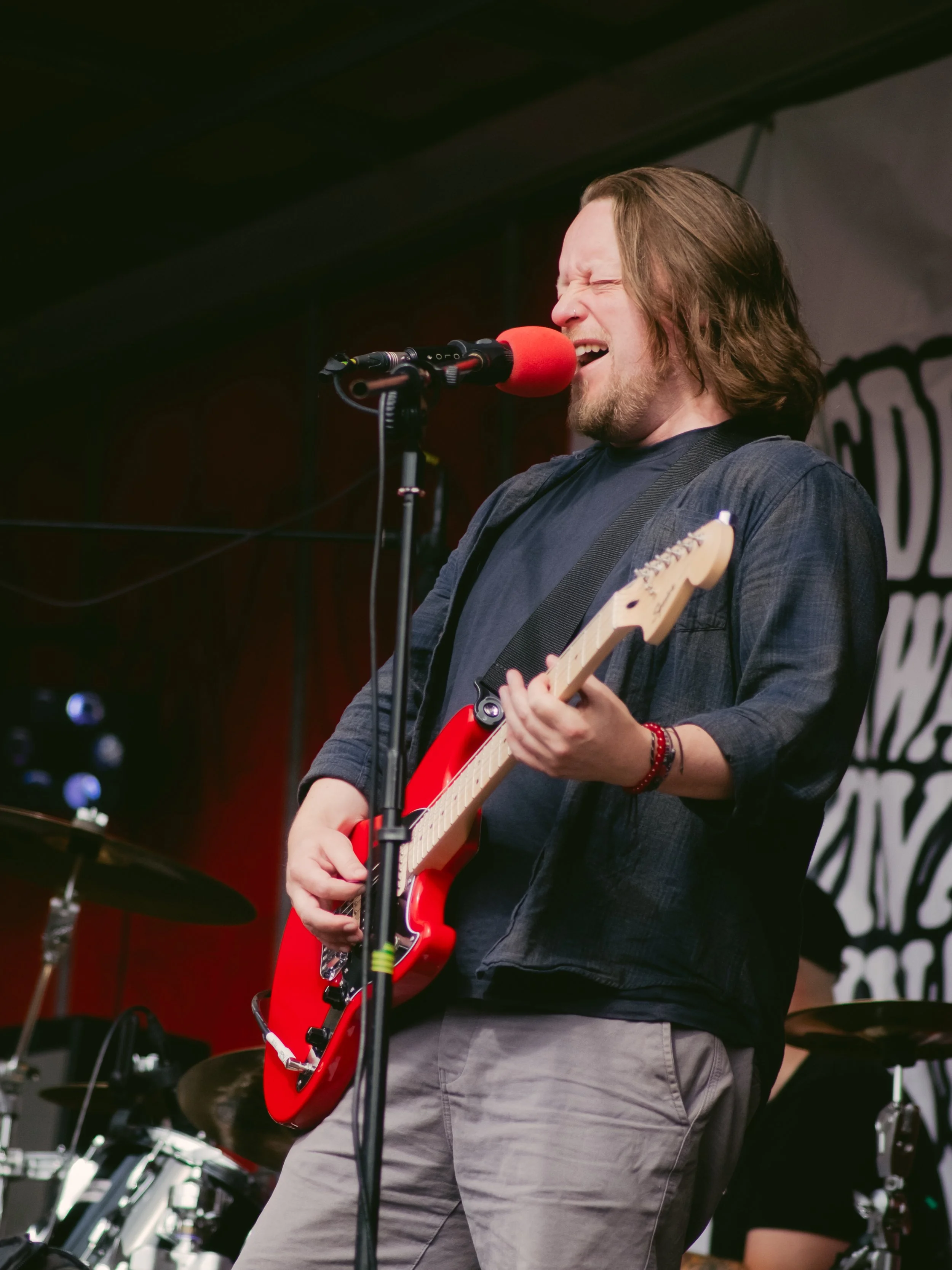 A man with long hair and a beard playing an electric guitar and singing into a microphone on stage.