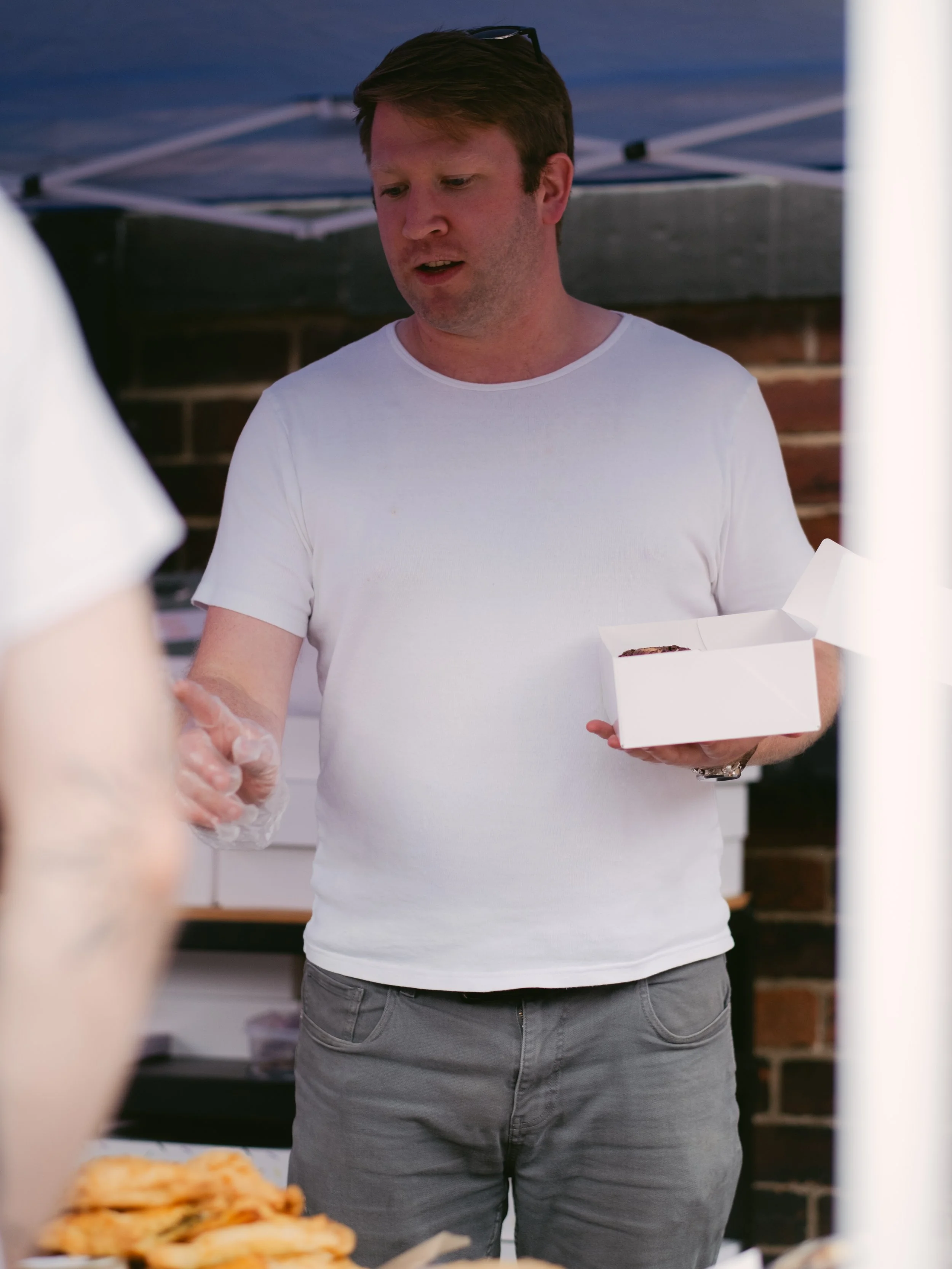 A man in a white t-shirt holding a takeout food box at an outdoor event