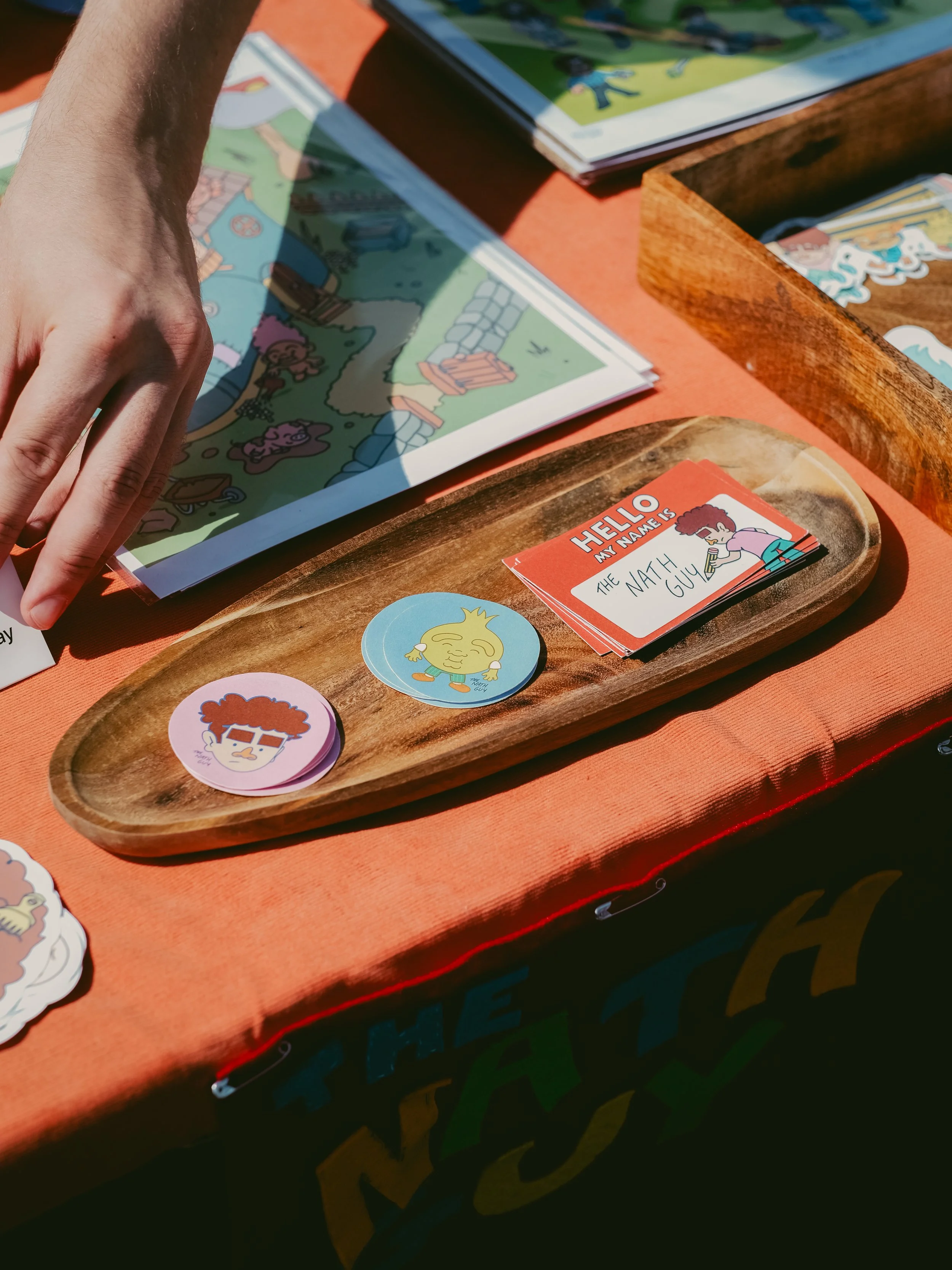 Colorful illustrated map on paper, sticker icons, and a name tag on a wooden tray at an outdoor event table.