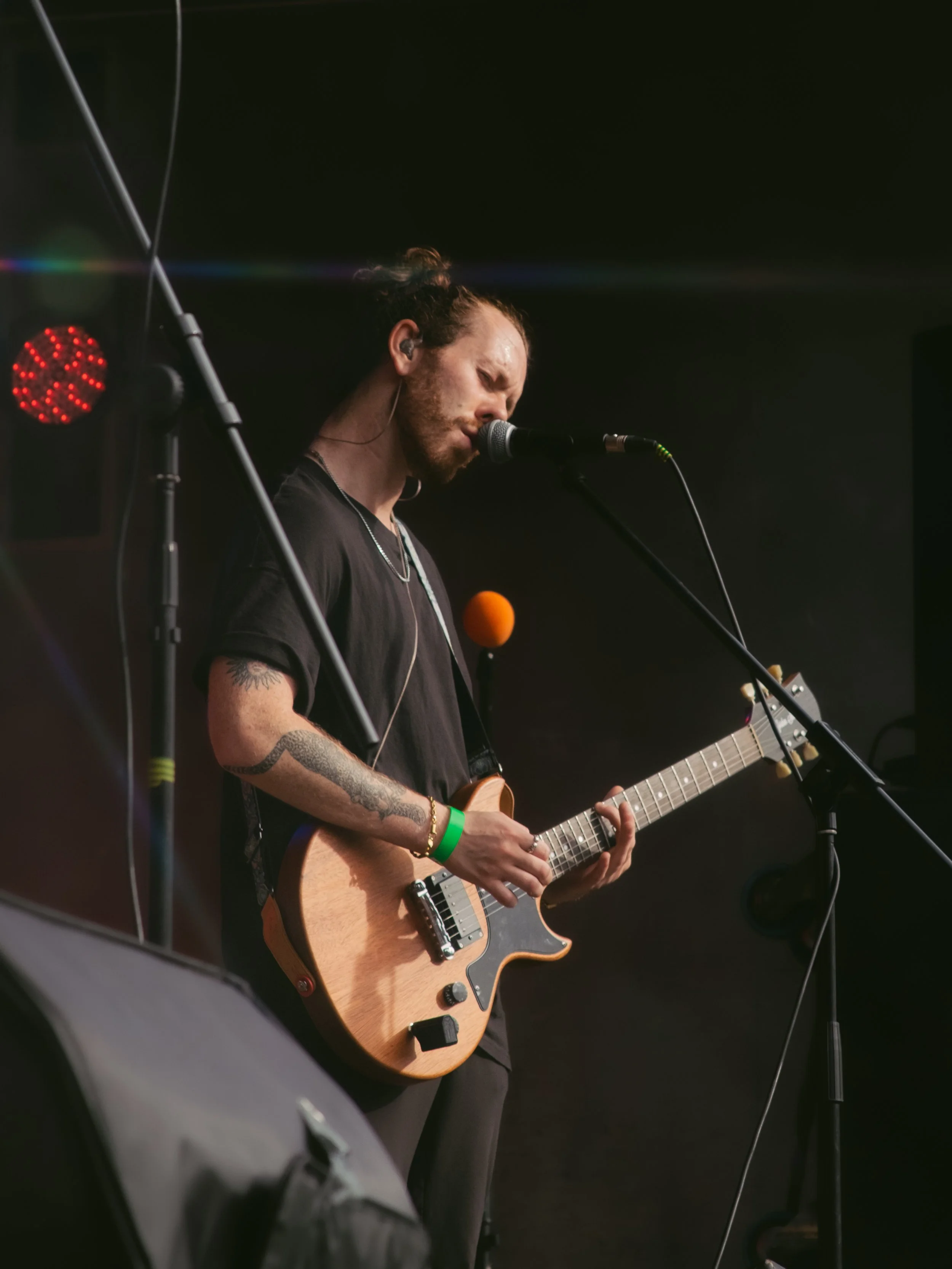 A musician playing an electric guitar and singing into a microphone on stage, with red and blue stage lights.