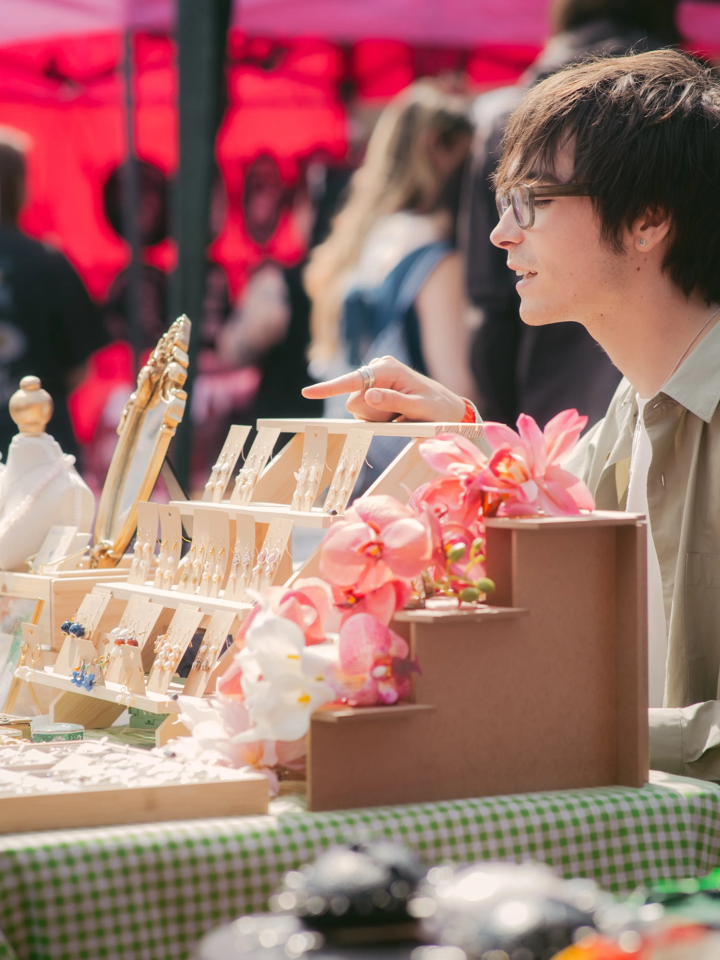 A person shopping at an outdoor market stall selling jewelry and artificial flowers.