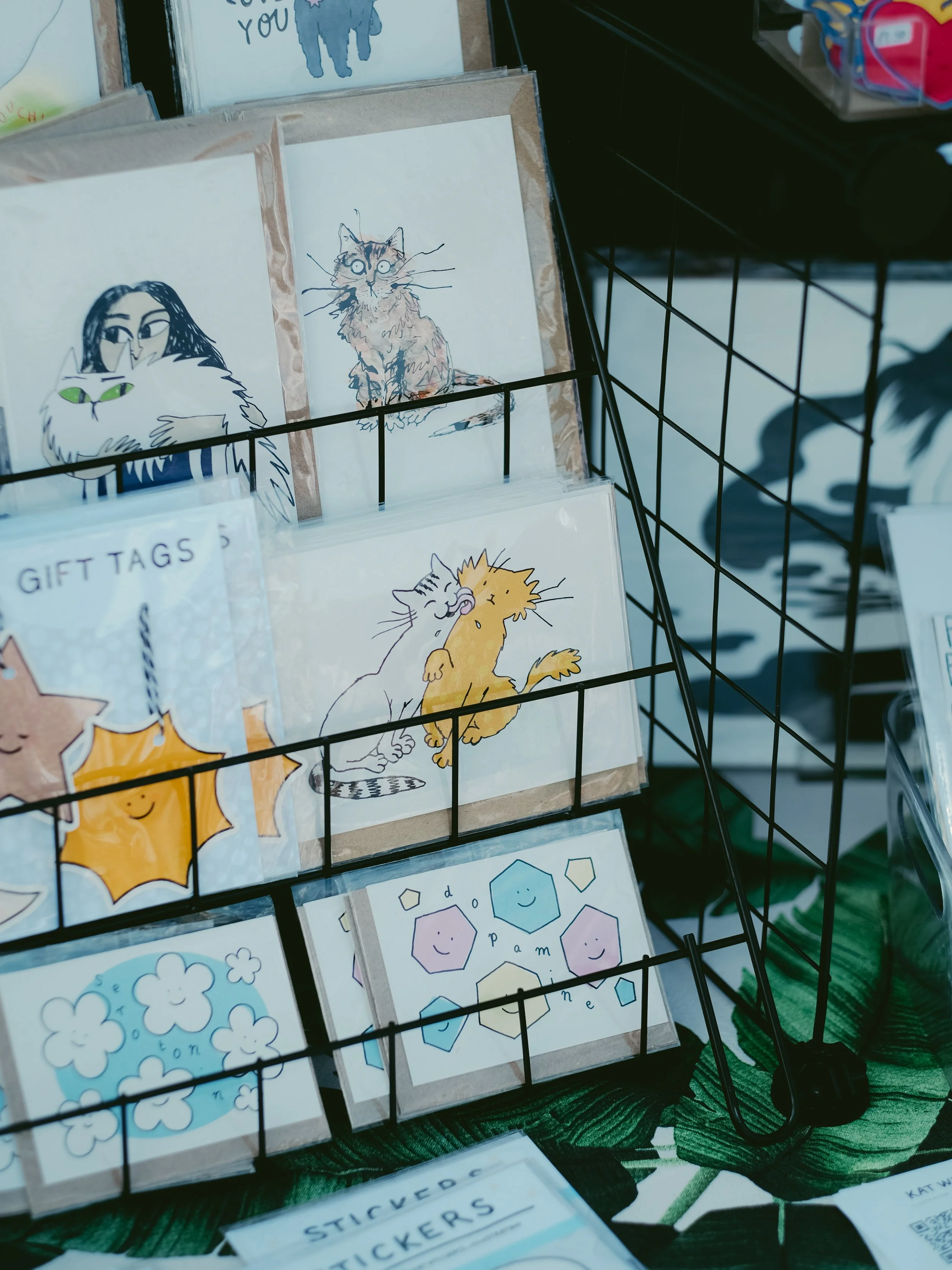 A display rack holding illustrated greeting cards with various cat and floral designs.