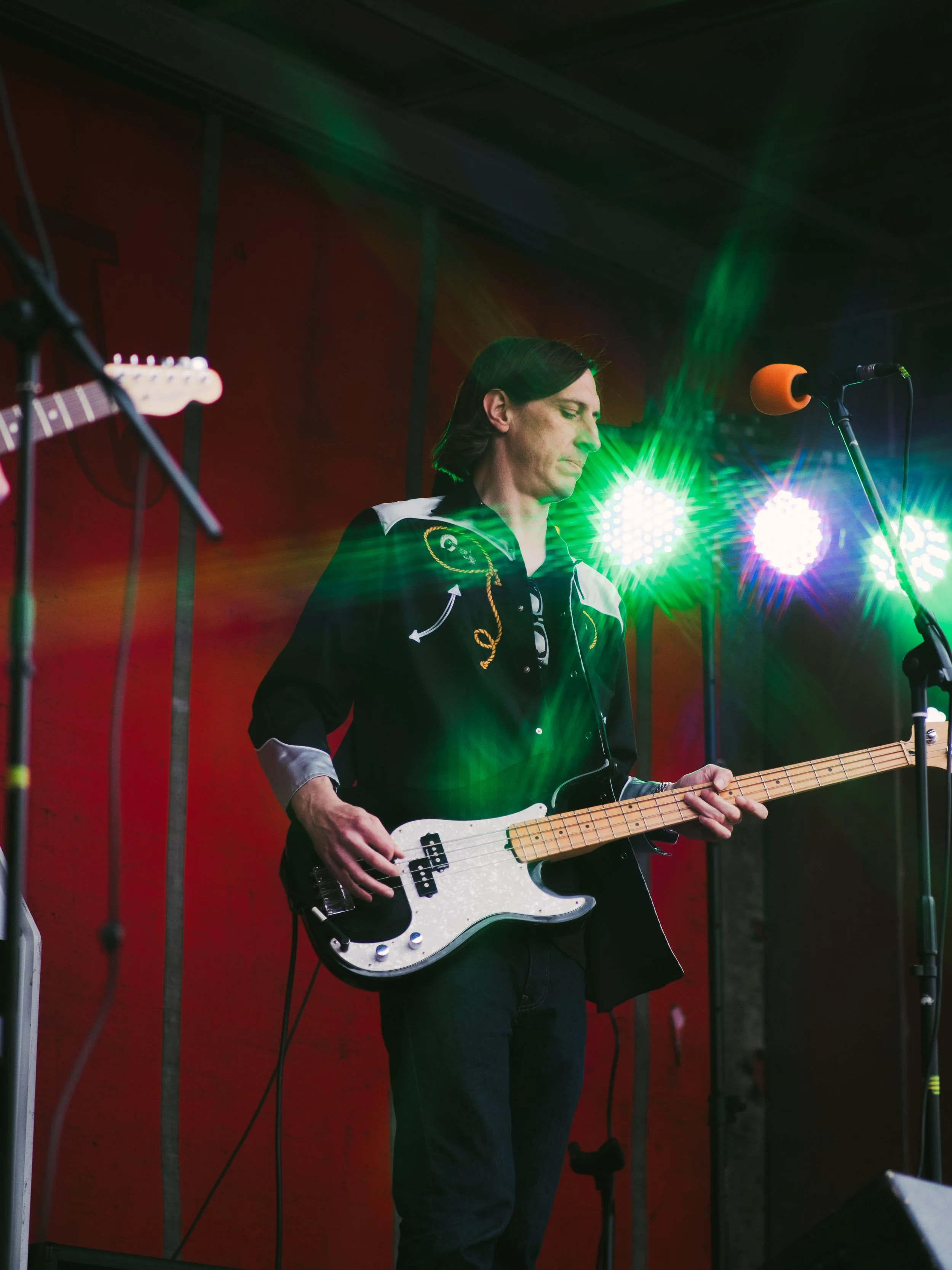 A musician playing an electric bass guitar on stage with green stage lighting.