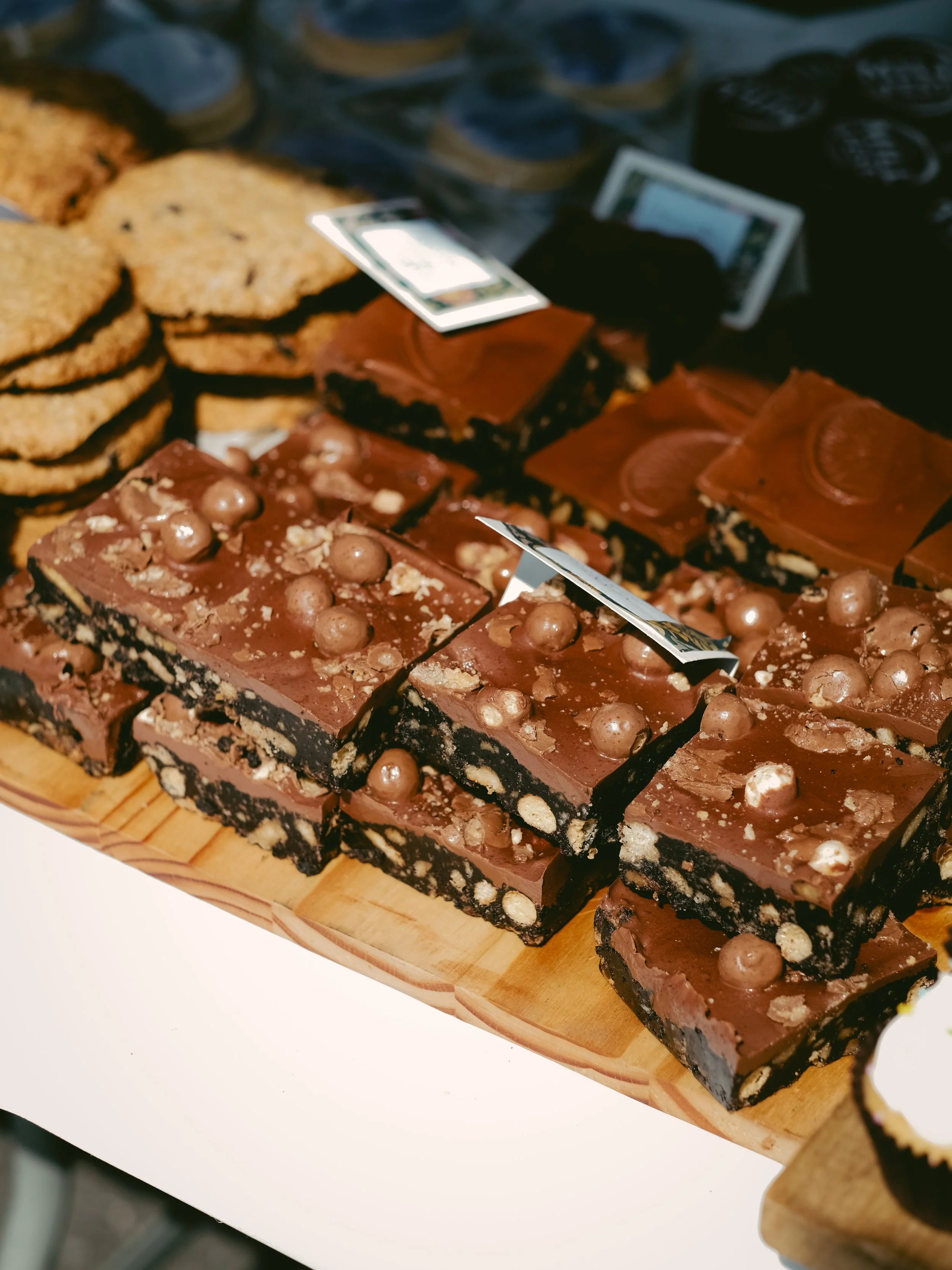 Assorted chocolate brownies with chocolate balls on top and cookies on the side, displayed on a wooden tray.
