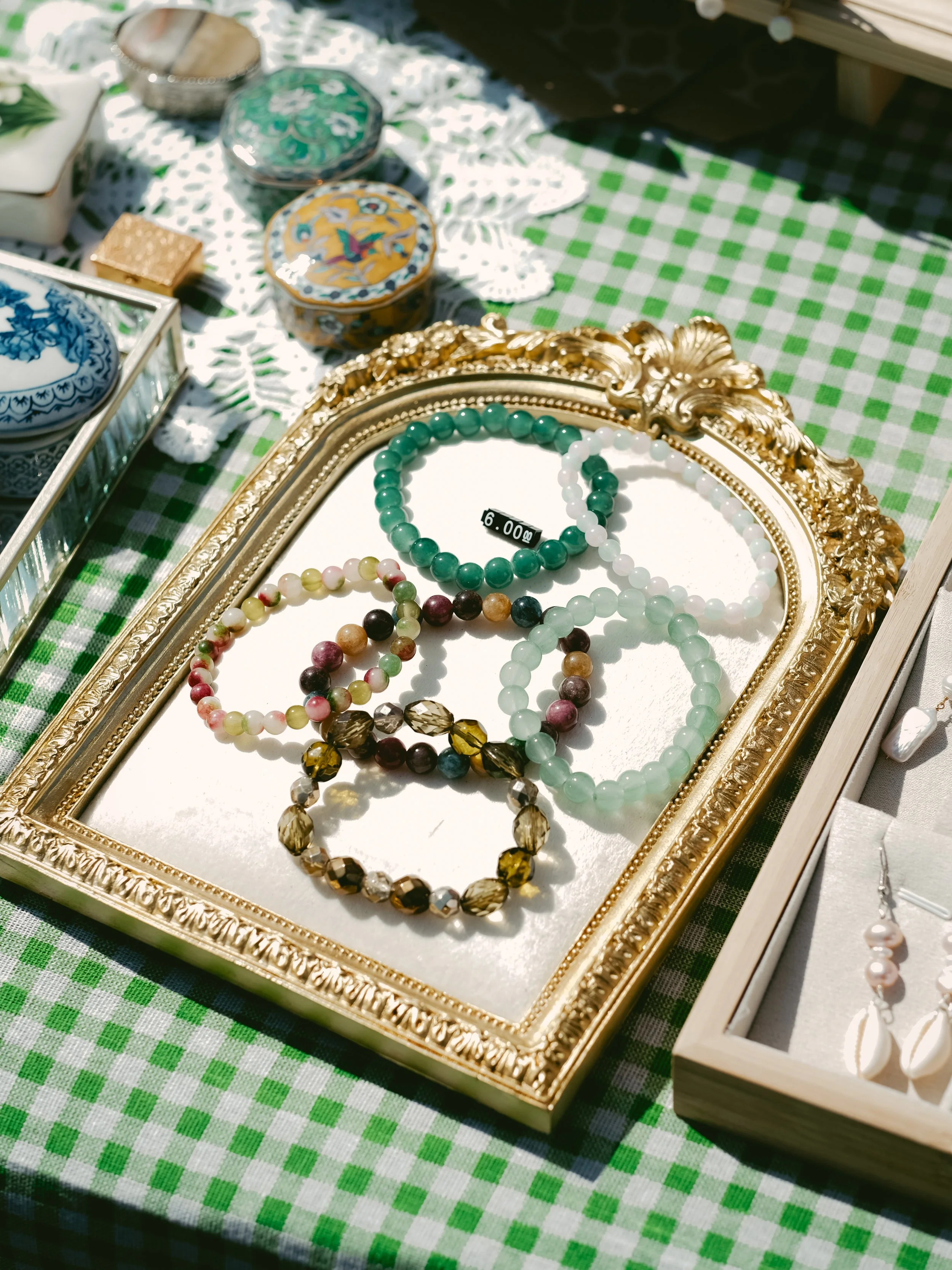 A decorative display of colorful beaded bracelets on a gold ornate tray, set on a green and white checkered tablecloth at an outdoor market.