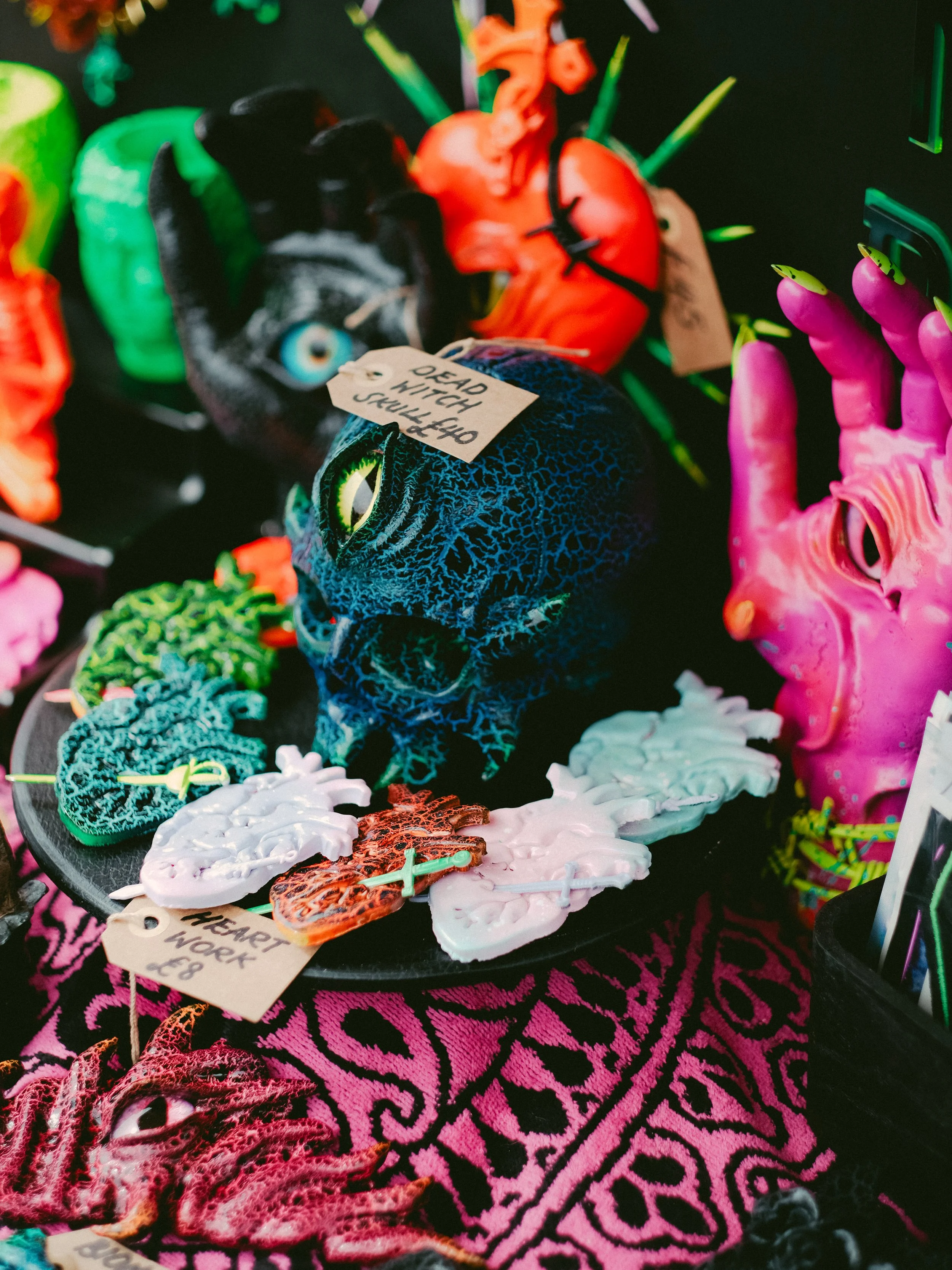 A display of brightly colored Halloween decorations including a black cat, a blue skull, pink and orange demons, hearts, and other spooky-themed items.