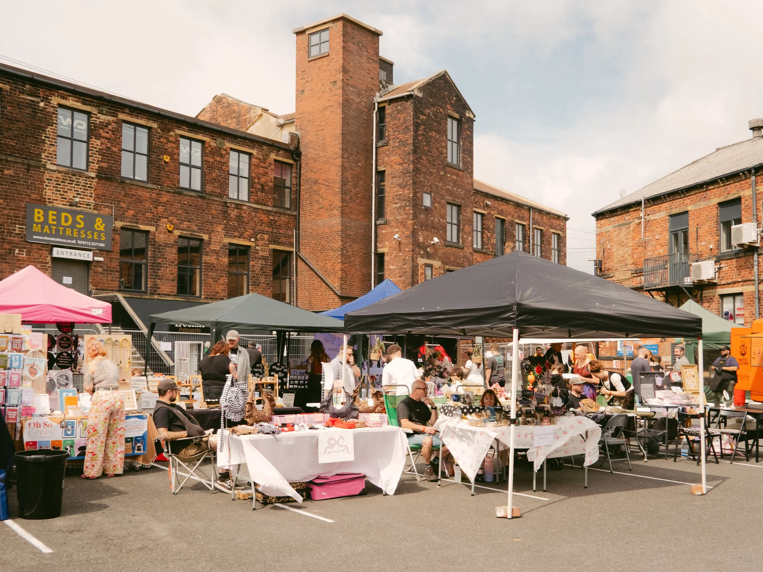Outdoor market with vendors under tents selling books, crafts, and jewelry in front of brick buildings.
