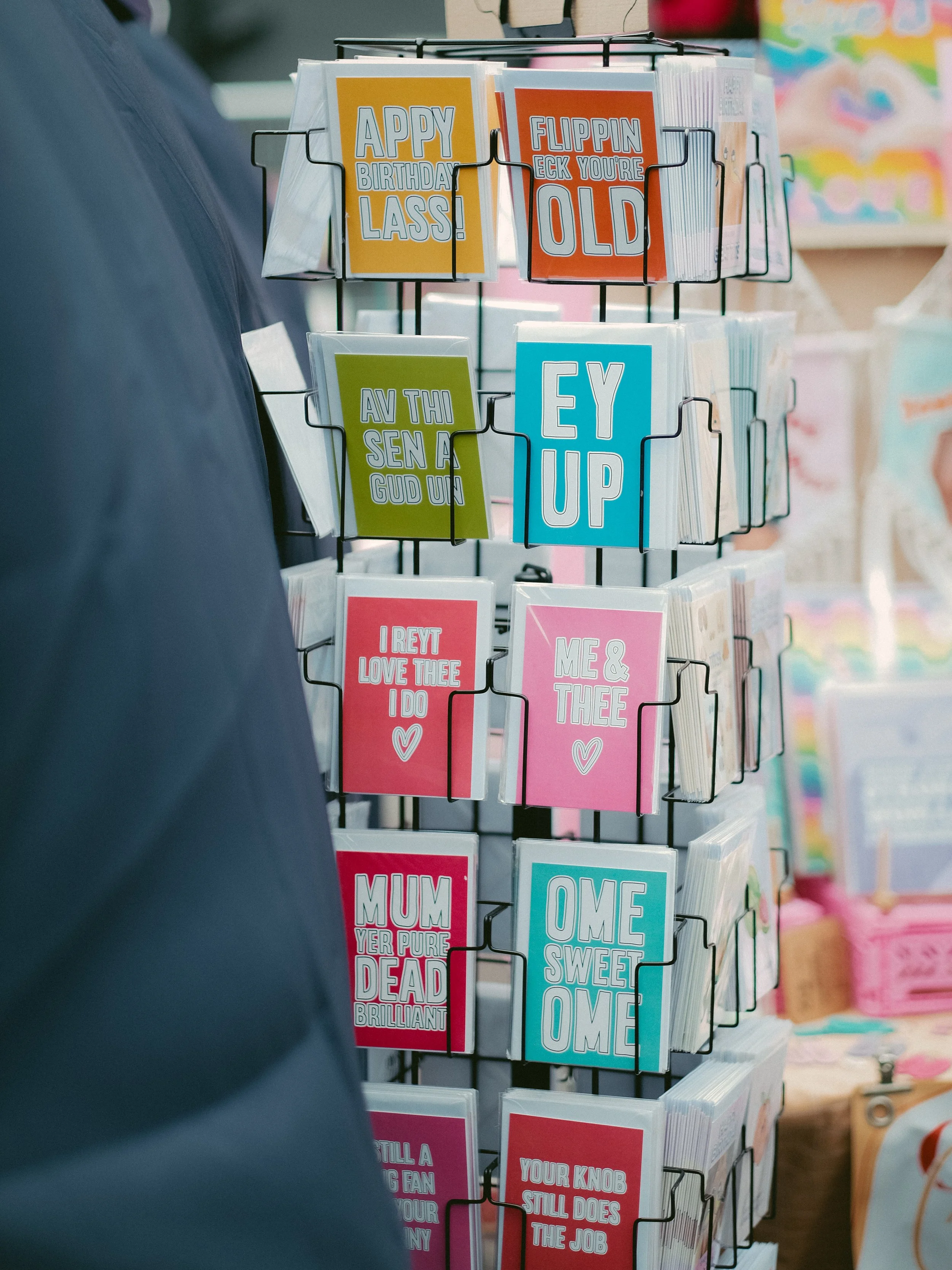 Stand of colorful greeting cards with humorous messages, arranged on a wire display rack.