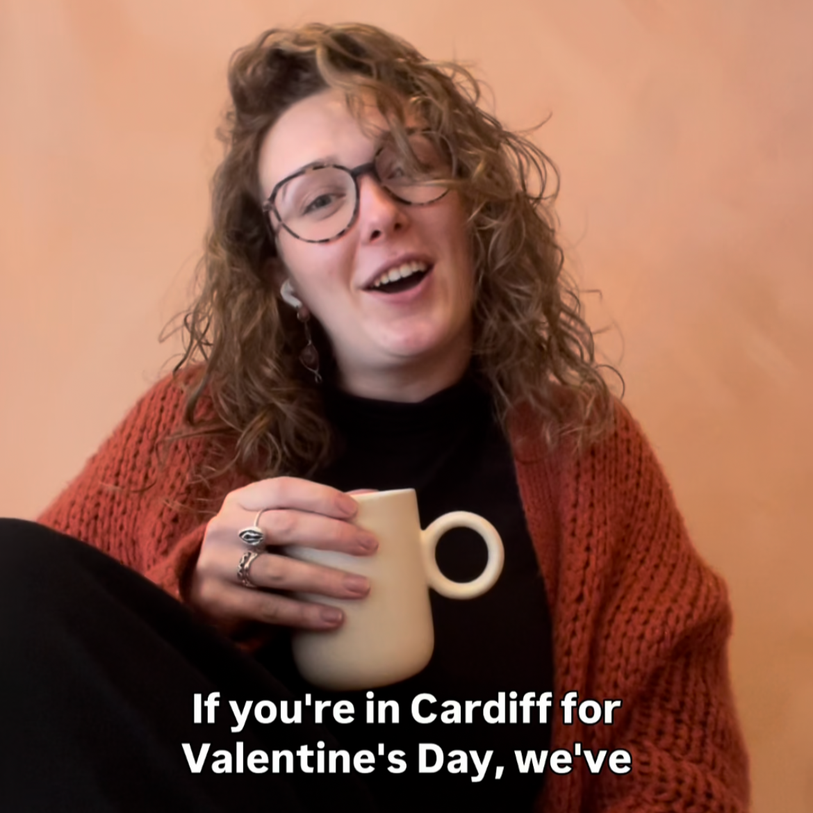 Sarah sat talking to the camera with a cup of tea. Autogenerated captions at the bottom of the image read "if you're in Cardiff for Valentin'e Day, we'.ve..."