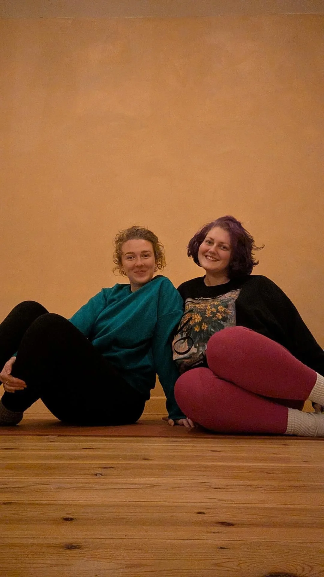 Two Yoga teachers sat on a mat smiling