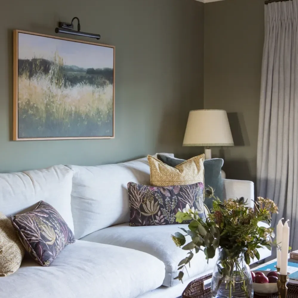 Living room with a white sofa adorned with patterned pillows, a glass vase with flowers, and a side table with candles and fruit. By Michelle Shakallis Interiors, Award-Winning Interior Designers for Kent and London