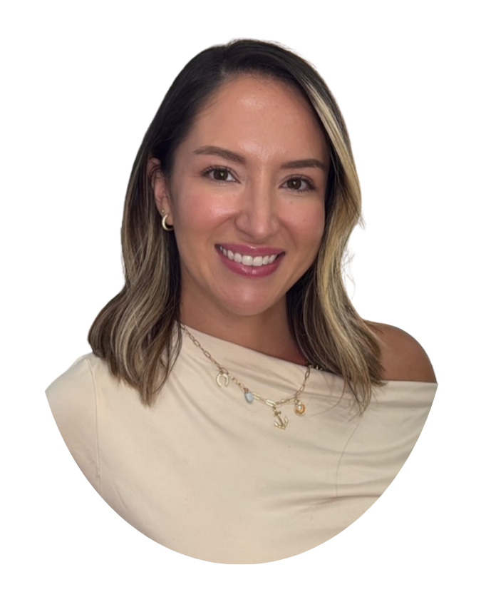 A smiling woman with shoulder-length brown hair and blonde highlights, wearing a cream-colored top off her shoulder and layered gold necklaces with charms.