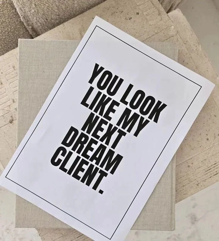 A printed quote that says, "You look like my next dream client," placed on top of a beige surface next to a light gray cloth.