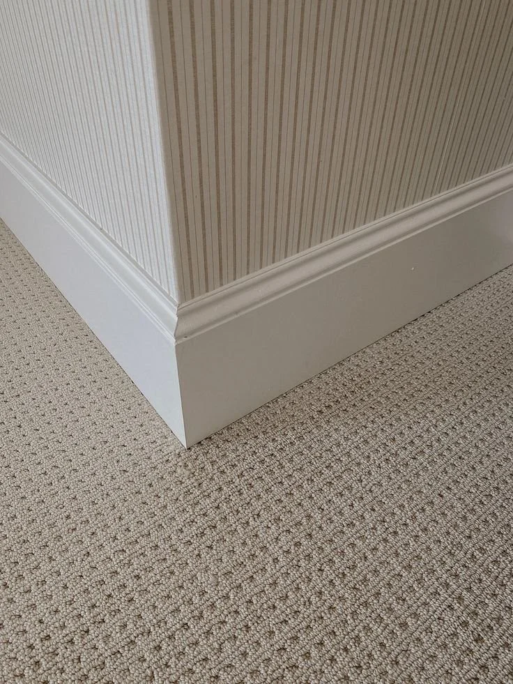 Close-up of a corner of a room showing baseboards, carpet, and a wall with striped wallpaper.