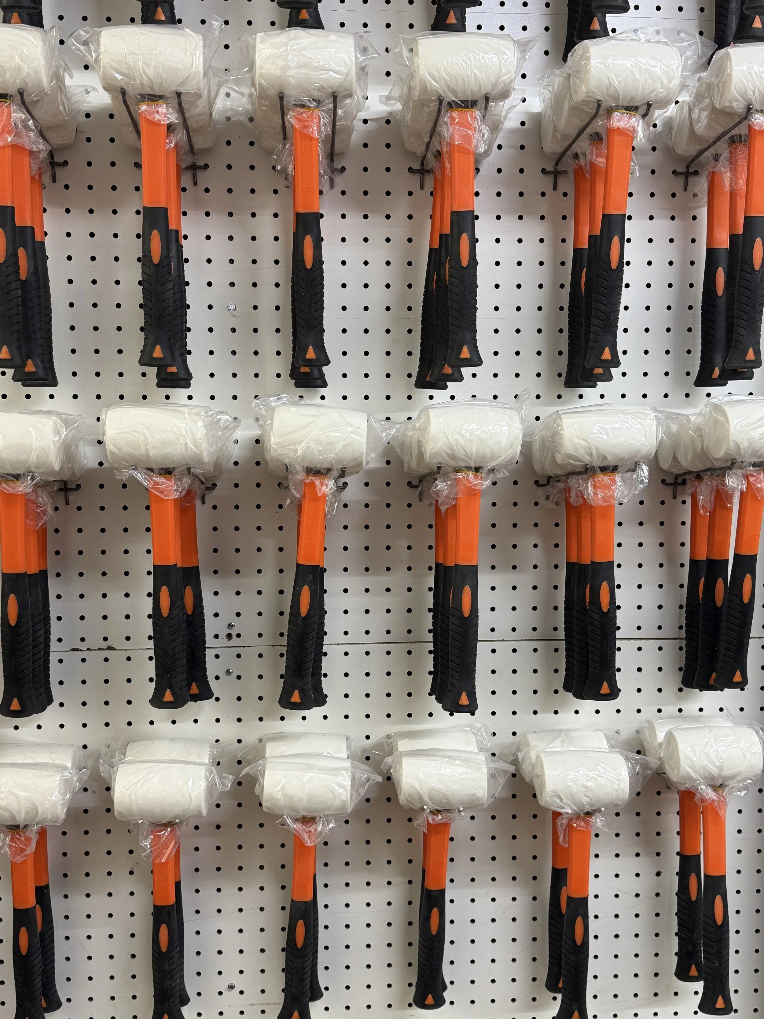 A display of foam mallets with black and orange handles hanging on a pegboard.