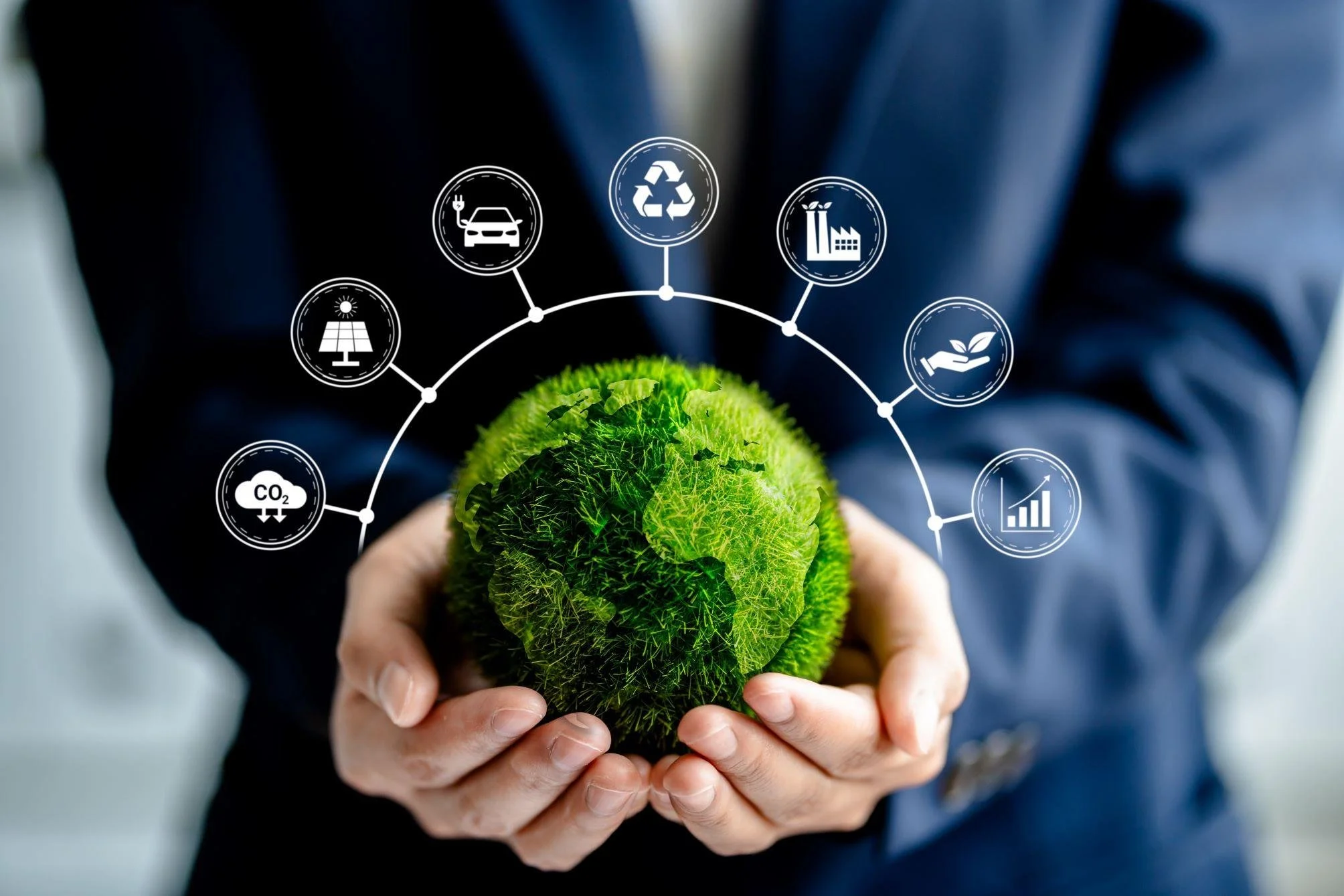 Person in business suit holding a green globe with digital icons representing solar energy, CO2 reduction, recycling, electric vehicle, factory emissions, sustainability, and environmental impact surrounding it.