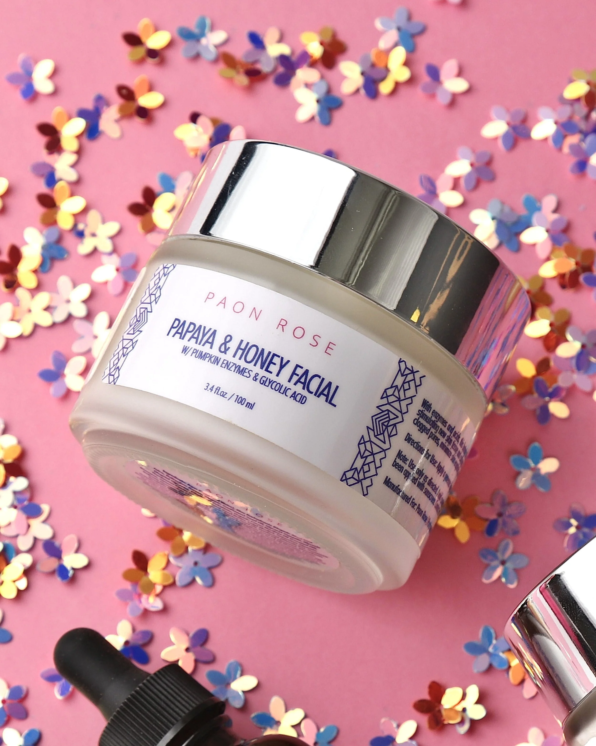 Jar of Paon Rose Papaya and Honey Facial cream with colorful flower-shaped confetti on pink background.