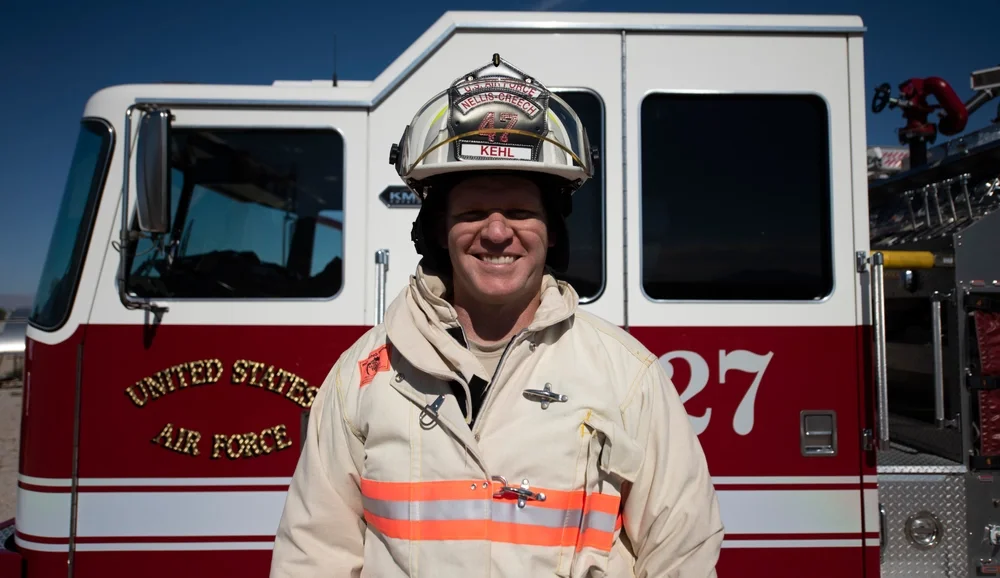 A firefighter in uniform and helmet standing in front of a United States Air Force fire truck.