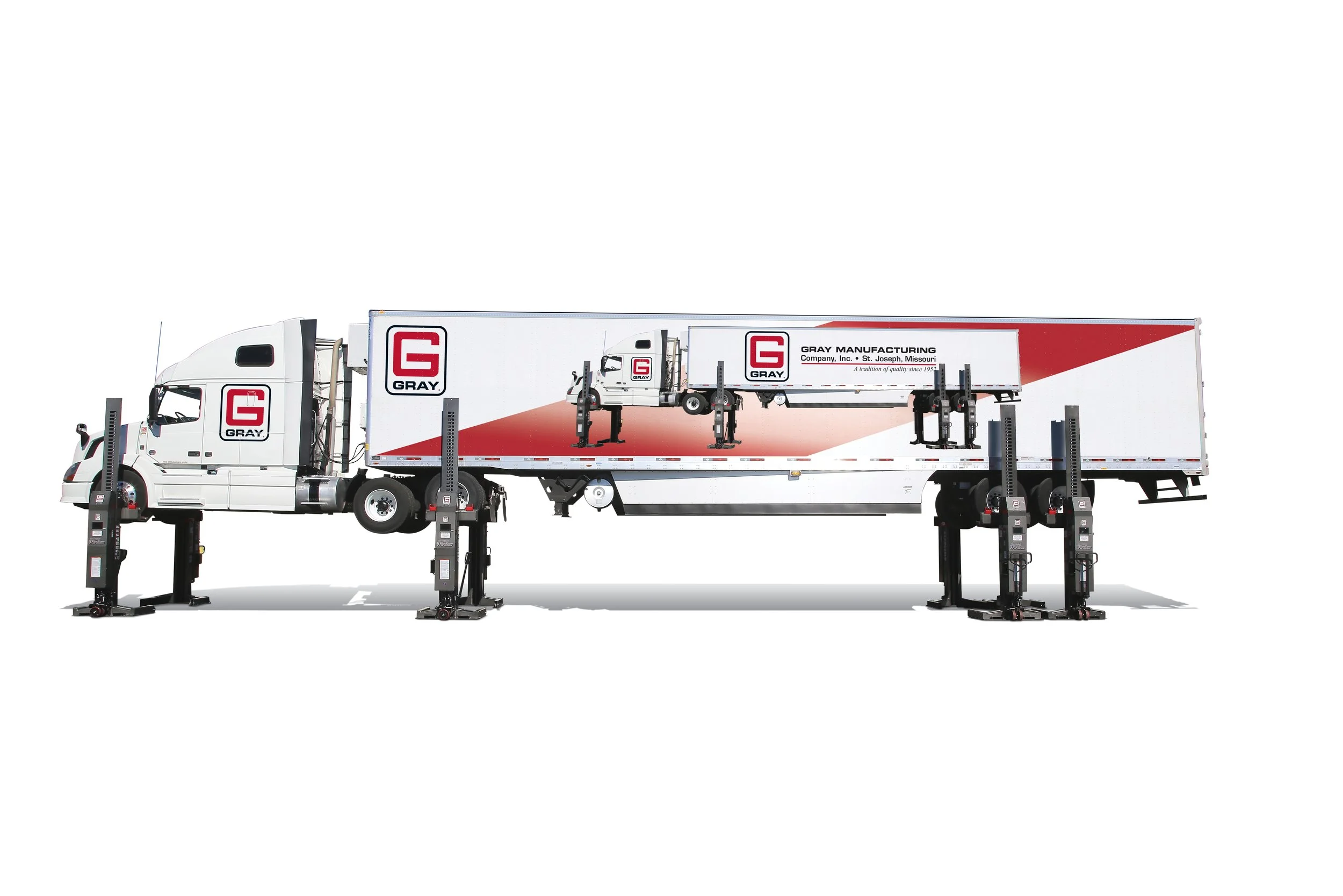 A white semi-truck with signage for Gray Manufacturing, equipped with multiple jacks and lifting equipment for vehicle repairs or maintenance.