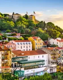Colorful houses with a castle on a hill in the background, lush greenery, and a clear sky.