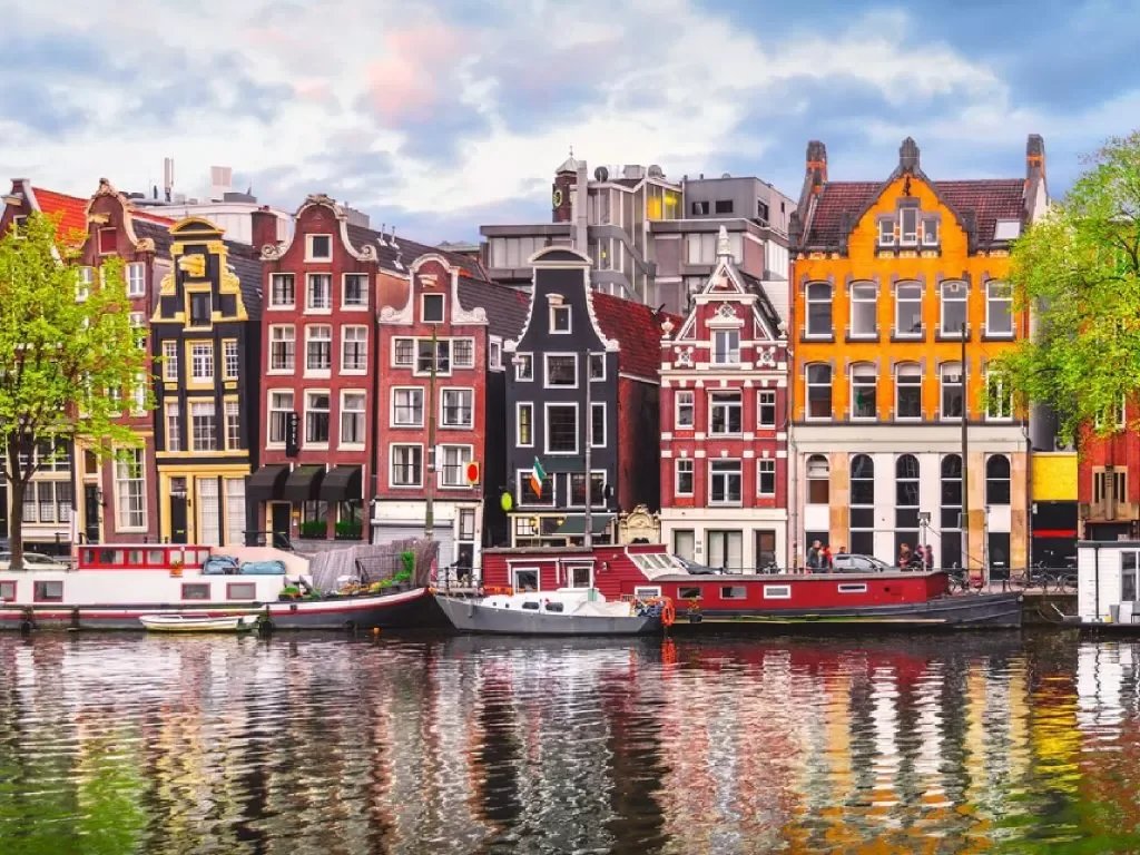 Colorful historic buildings along a canal with boats, in Amsterdam, Netherlands.