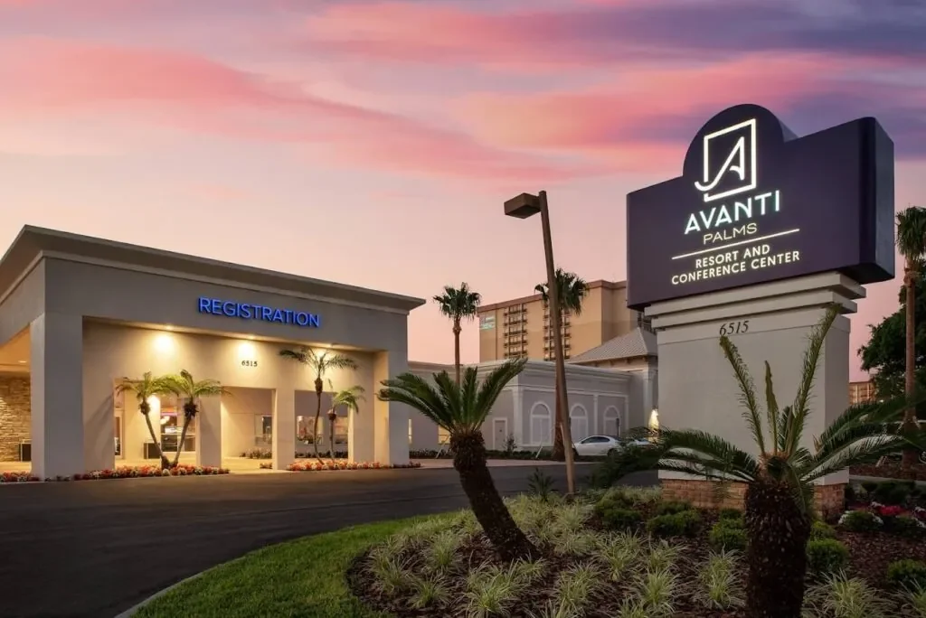 Entrance to Avanti Palms Resort and Conference Center at sunset with palm trees, a registration building, and a large sign displaying the resort's name.