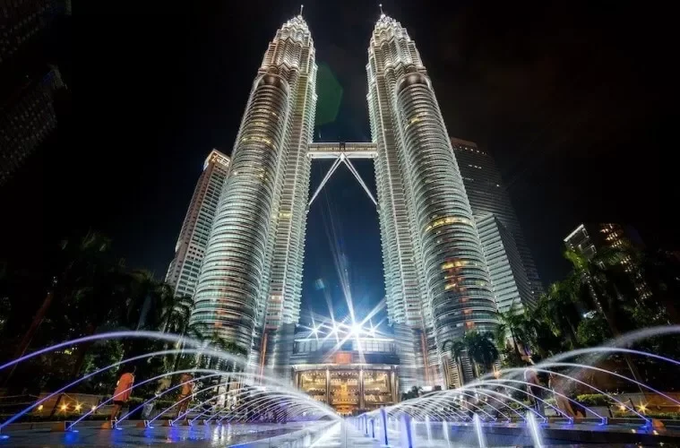 Nighttime view of the illuminated Petronas Towers in Kuala Lumpur, Malaysia, with a fountain in the foreground.