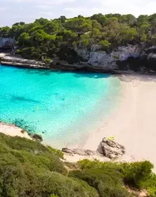 A secluded beach with white sand, turquoise water, and lush green trees surrounding the shoreline.