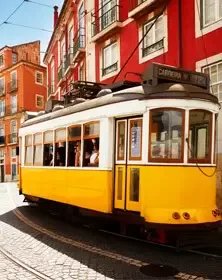 Yellow tram moving along a city street with colorful buildings in the background.