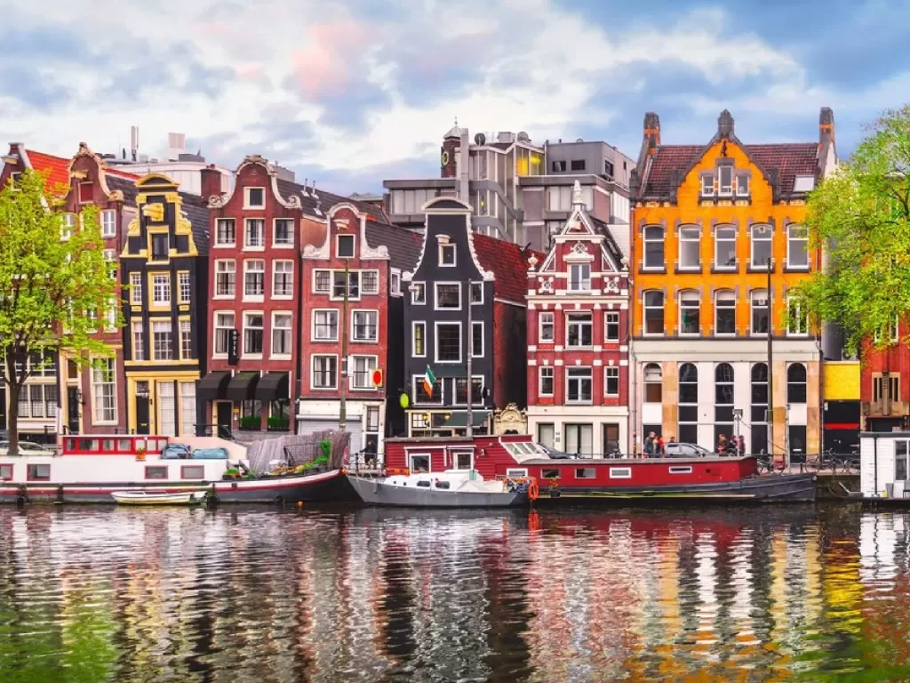Colorful row of historic Dutch-style houses along a canal with boat reflections in water.