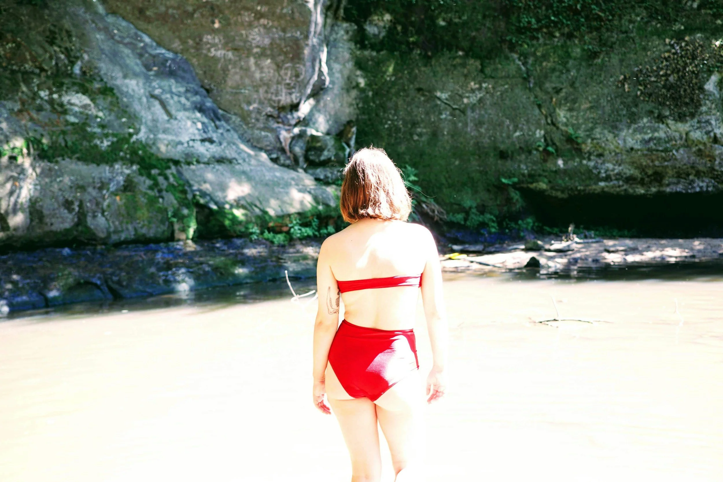 Woman walking towards a river while wearing a red bikini