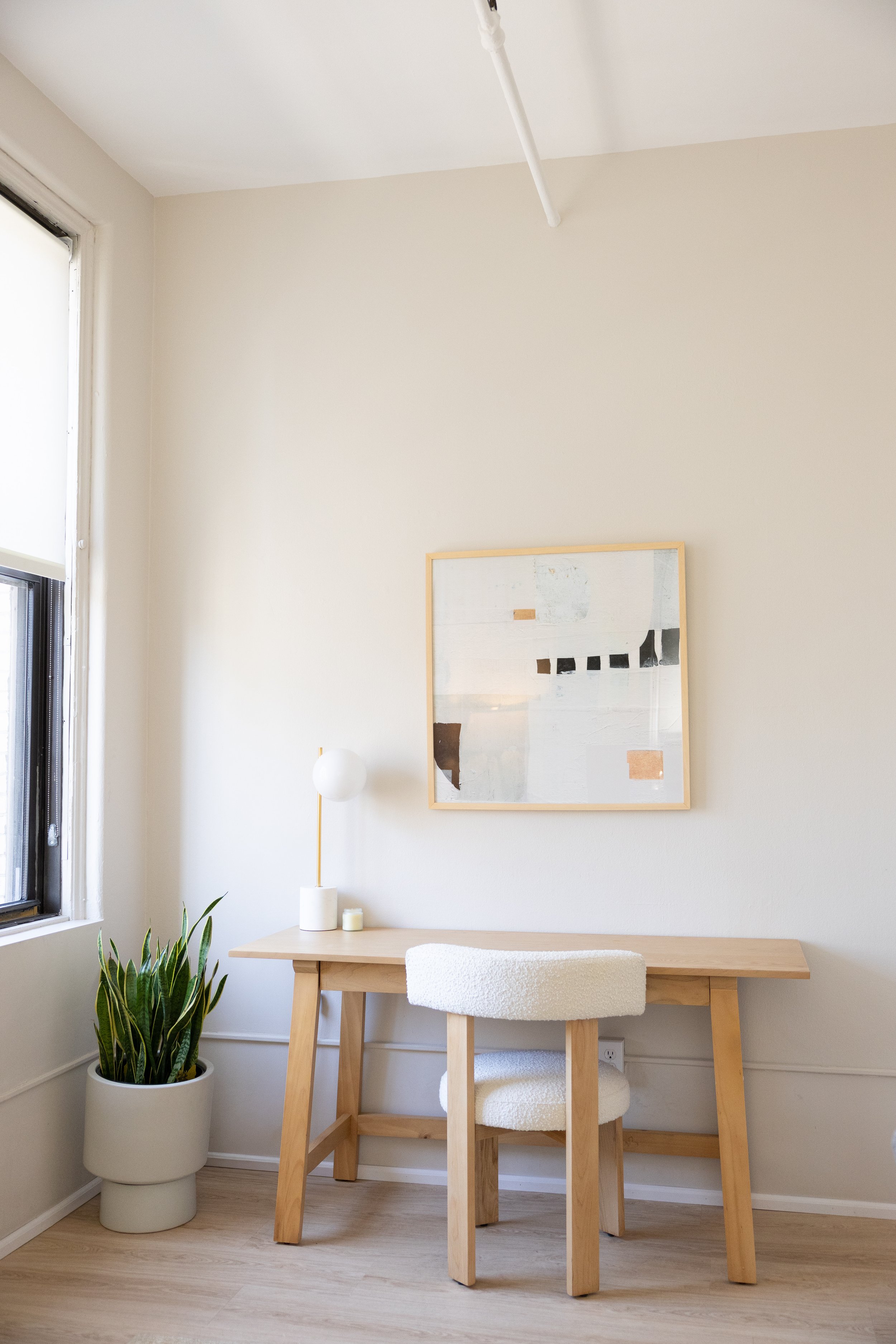 Therapist office with a cactus plant next to a light brown wooden desk with a lamp an abstract frame on the wall and a sherpa chair at Lindsey Turner Therapy