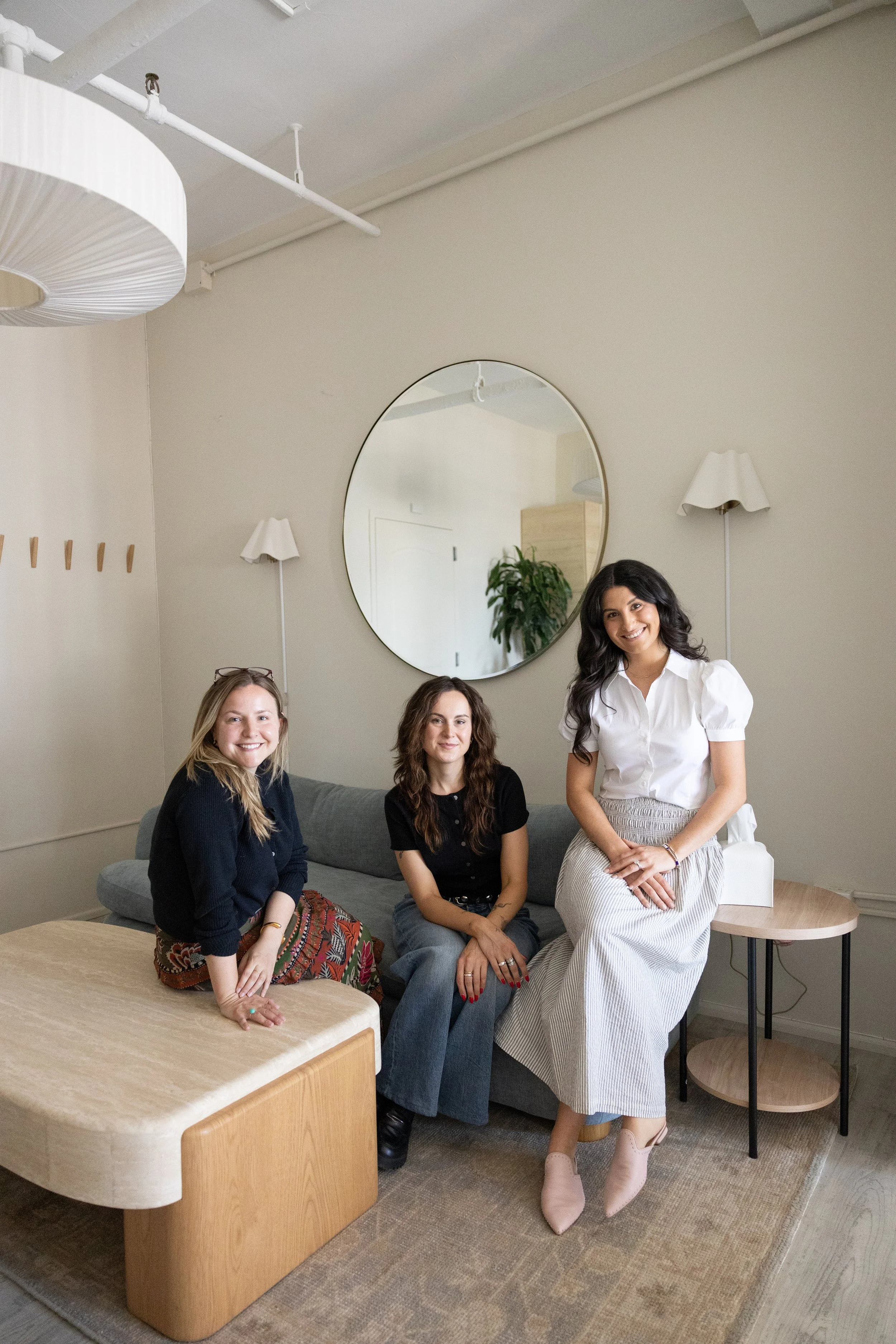Lindsey Turner and therapists sitting together on blue couch and a wooden coffee table, mirror on the wall reflecting a plant