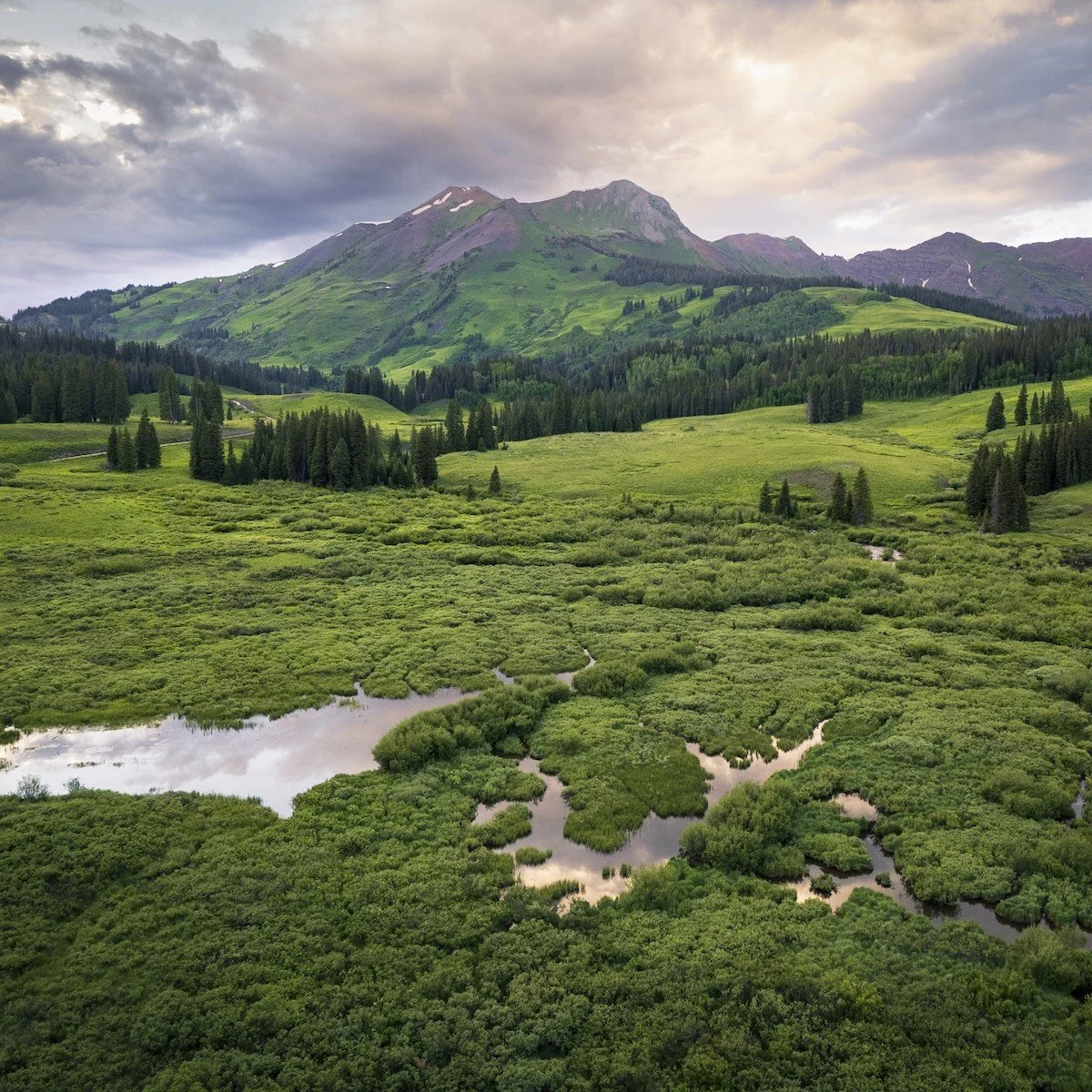 Scenic view of green mountains with a sky filled with clouds, dense forests, and marshy wetlands with small water bodies reflecting the sky.