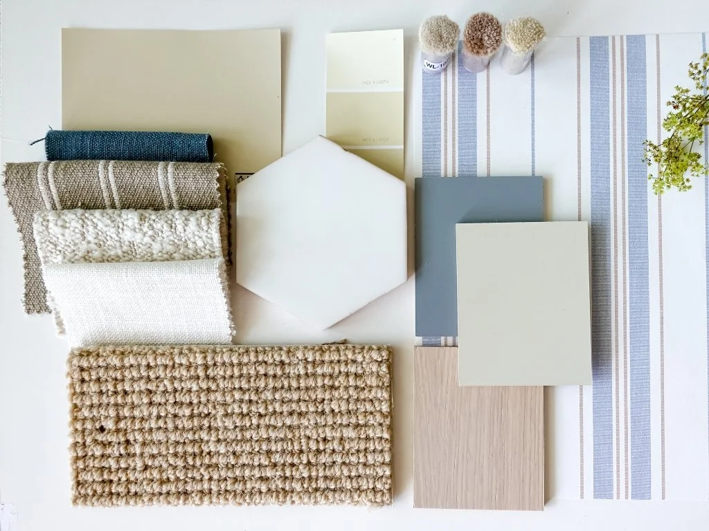 Interior design mood board featuring fabric swatches, carpet samples, paint chips, wood finish, and a hexagon tile arranged in a coastal-inspired neutral and blue palette.