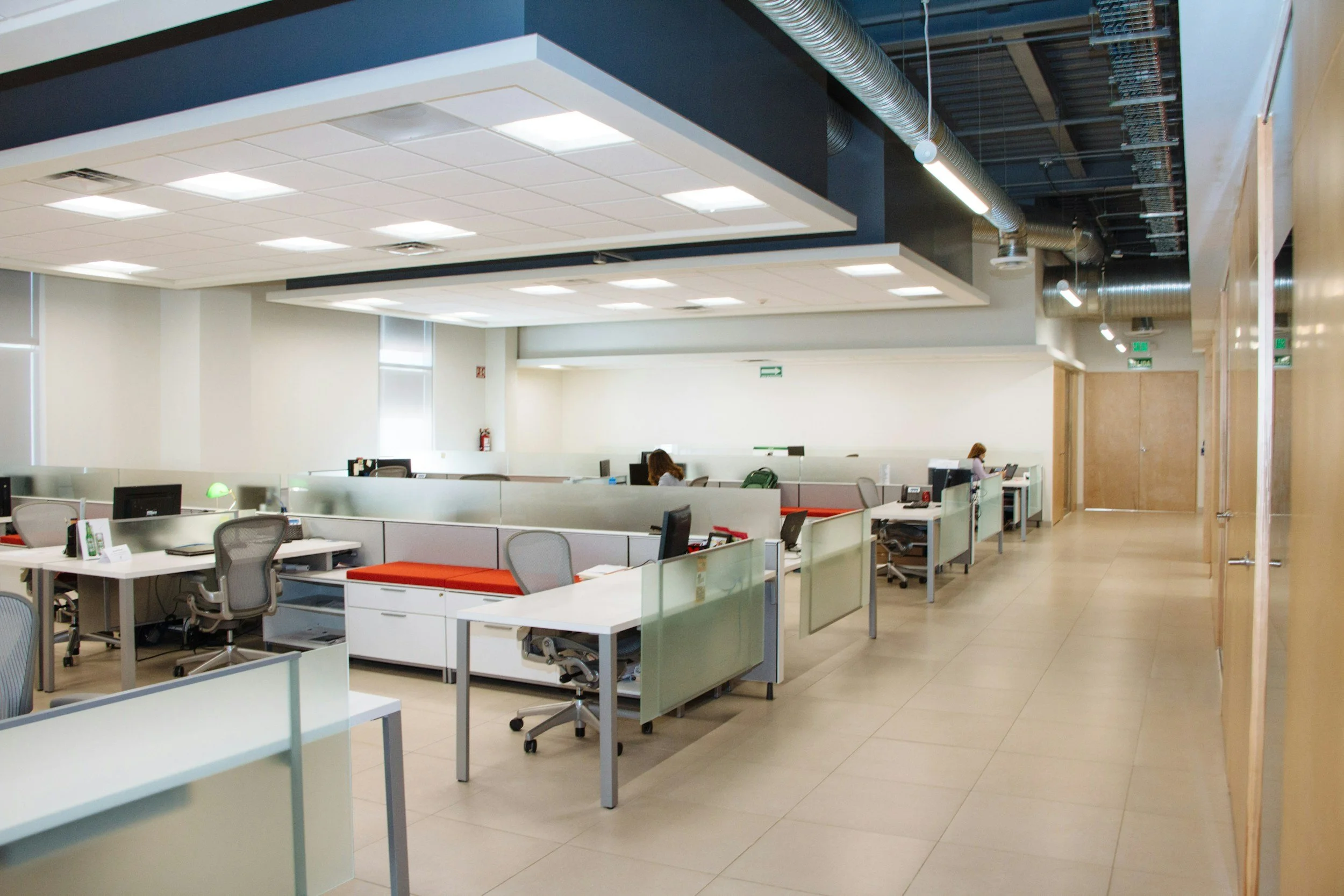 Empty office cubicles and workspaces with chairs, computers, and some people working.
