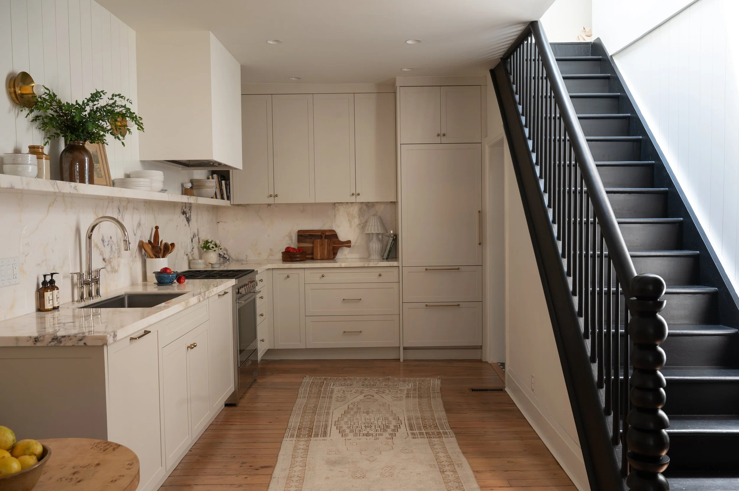 A modern kitchen with white cabinets, marble countertops, and black staircase railing.
