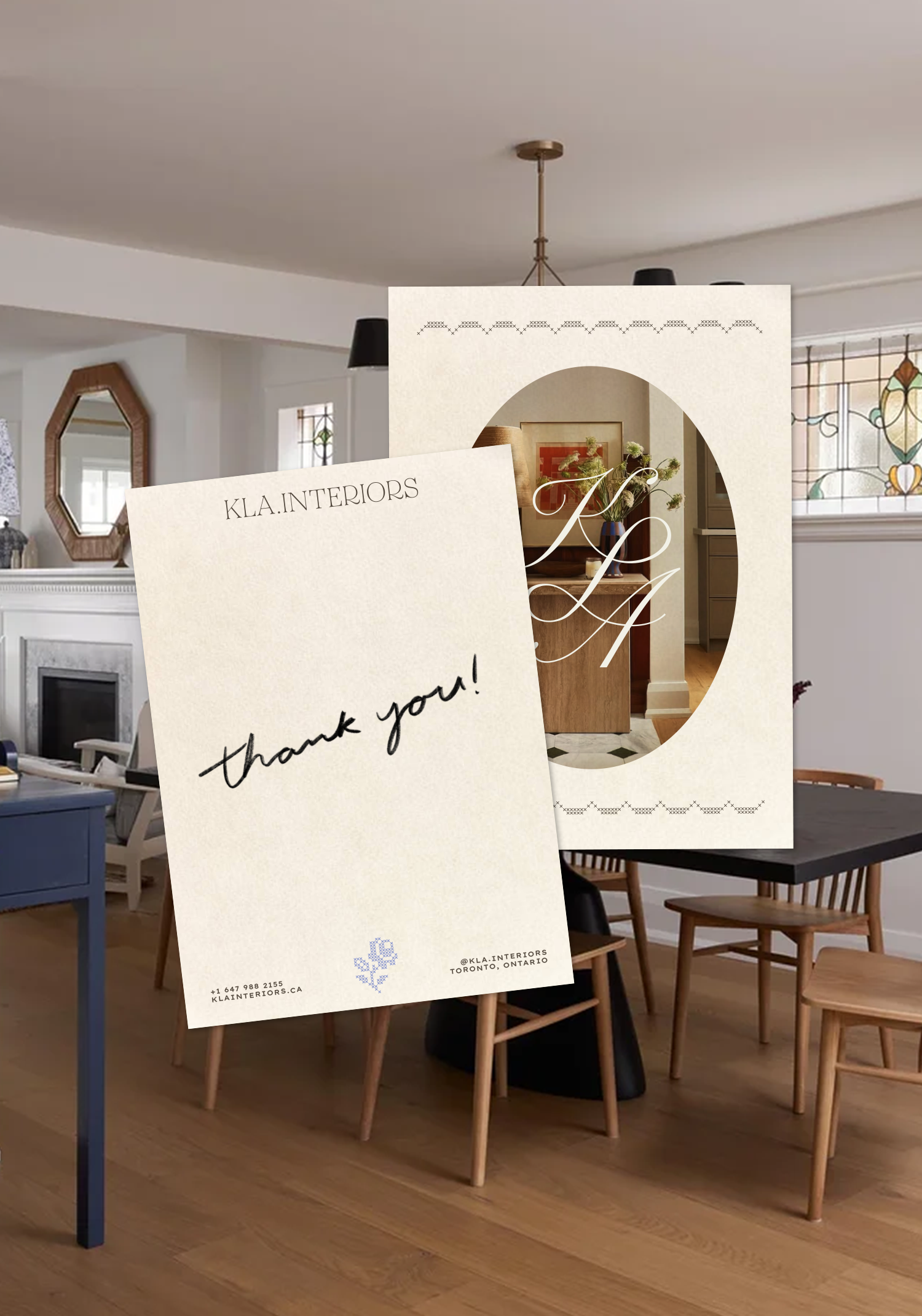 A thank you card from KLA Interiors placed on a dining table in a modern home interior with wooden chairs, a fireplace, and stained glass windows.