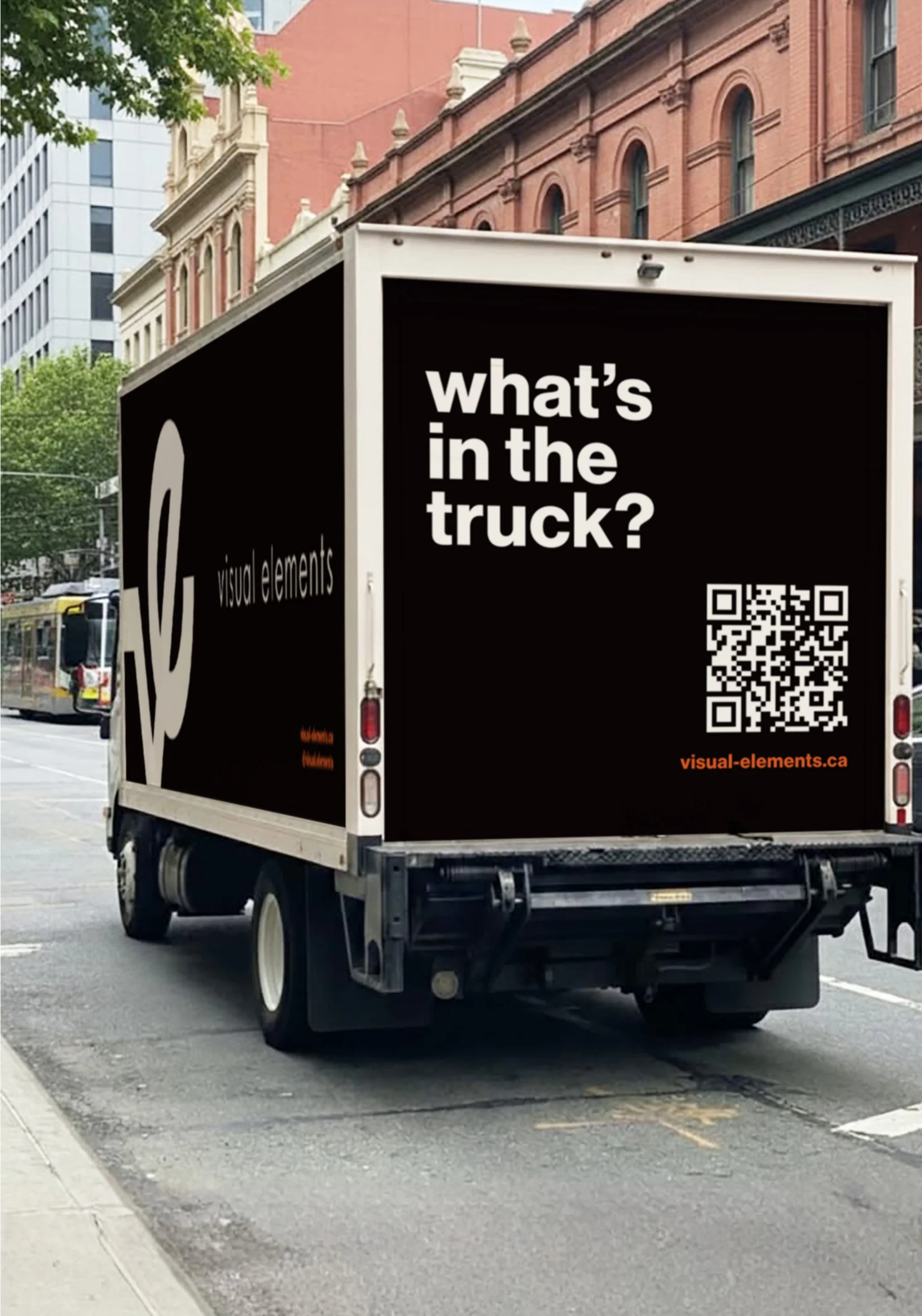 Black truck with a digital billboard on the back displaying the text 'what's in the truck?' and a QR code, parked on a city street with old brick buildings and modern glass buildings in the background.