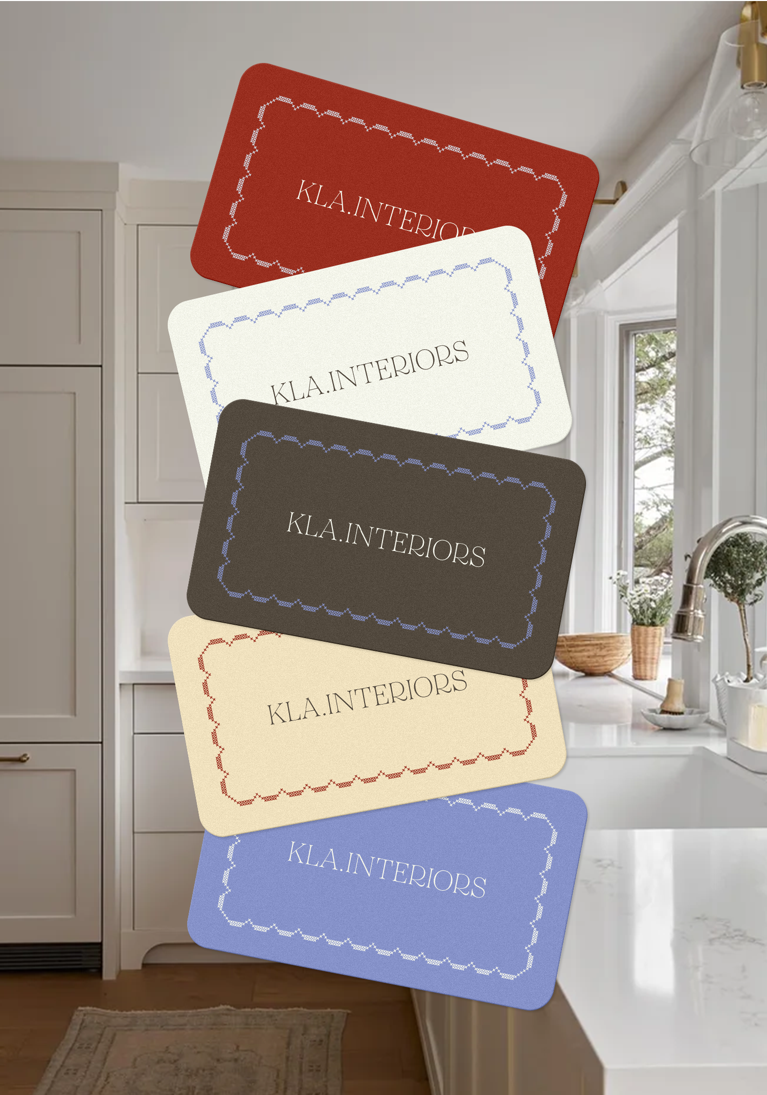 Multiple branded card samples in various colors, including red, white, black, beige, and blue, with the text "KLA.INTERIORS" displayed on each, positioned over a modern kitchen counter with cabinets and a window in the background.