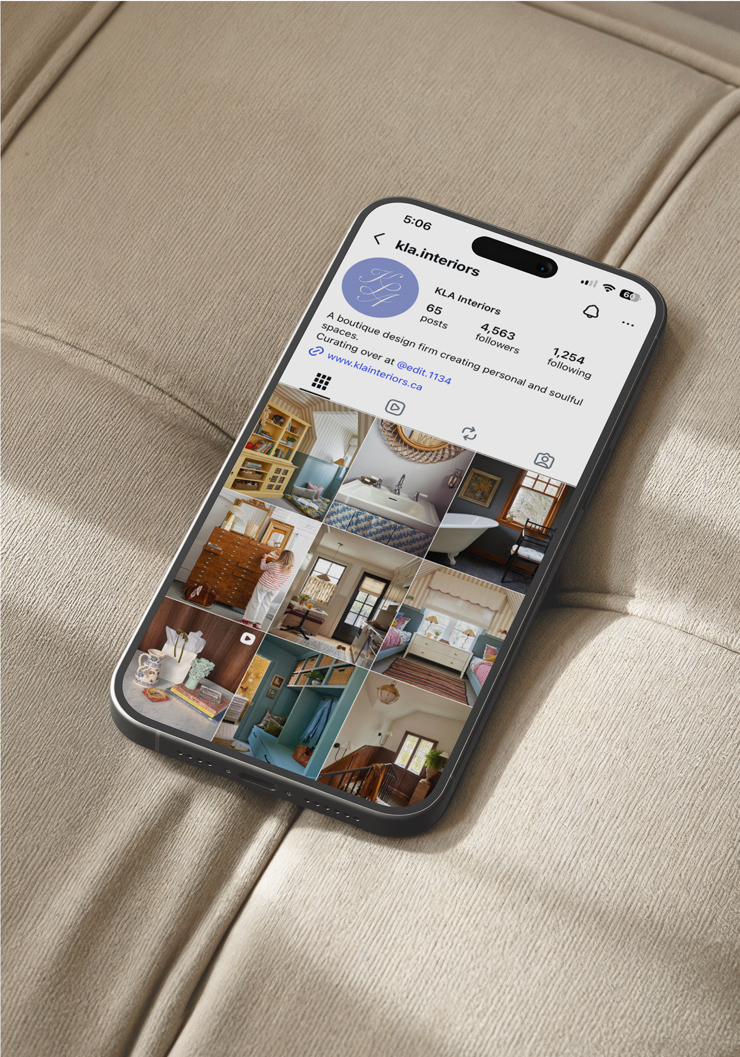 Close-up of a smartphone displaying an interior design firm's Instagram profile, resting on a beige fabric surface.