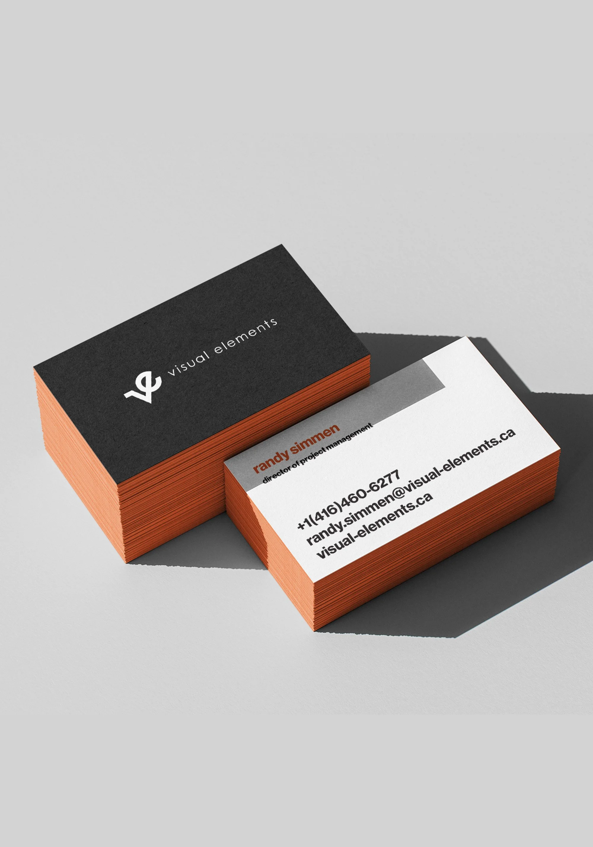 Business cards with black and white designs on a gray background. One card displays the name Randy Simmen, title, contact number, email, and website. The other card has a black background with white text that says 'visual elements' and a logo.