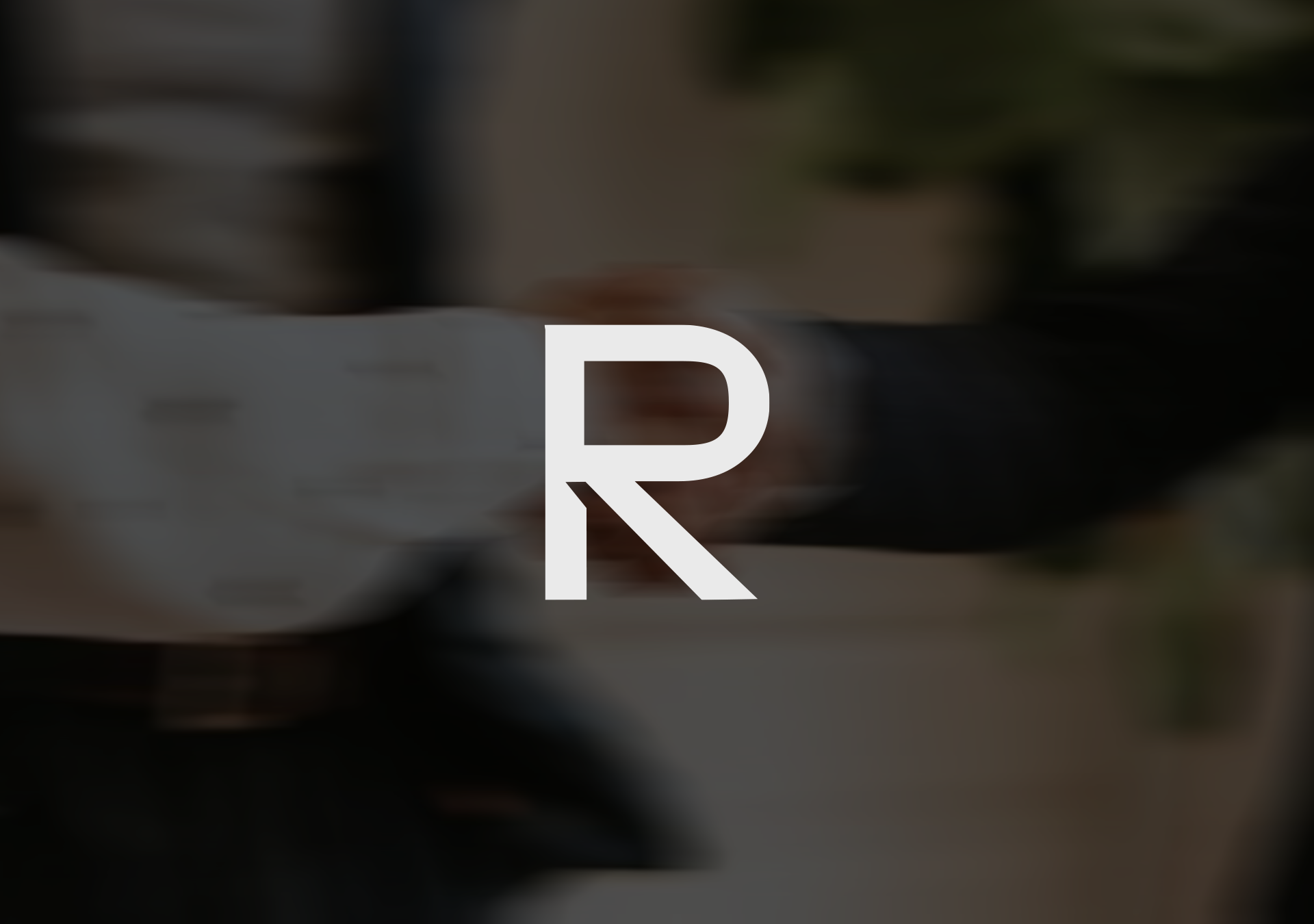 Blurred background with large white letter 'R' which is part of the Raiz&Co logo, overlayed in the center.