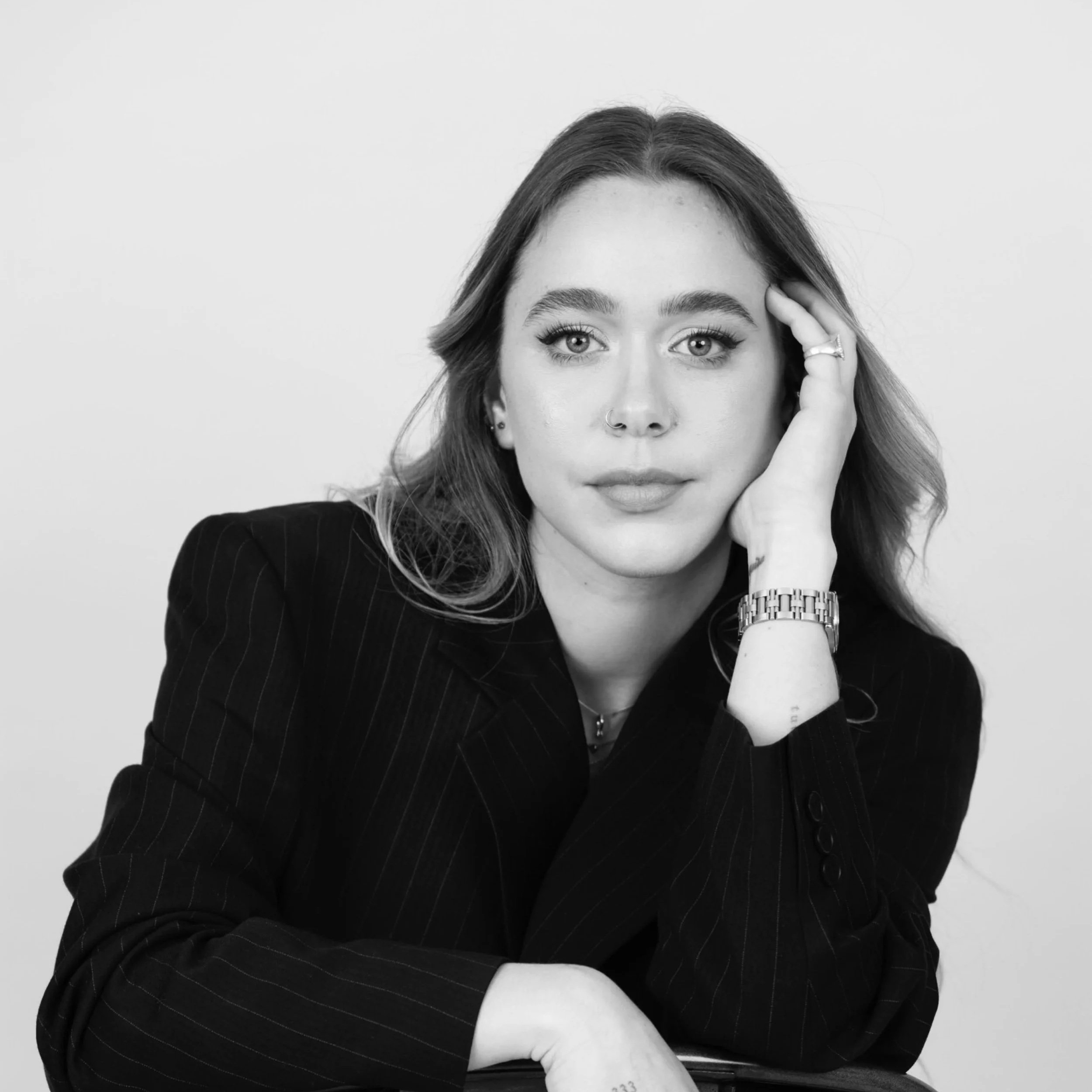 Black and white photo of a woman with long hair named Valentina Gomez, who is a managing partner at Raiz&Co, wearing a dark pinstripe blazer, resting her chin on her hand, and looking directly at the camera.