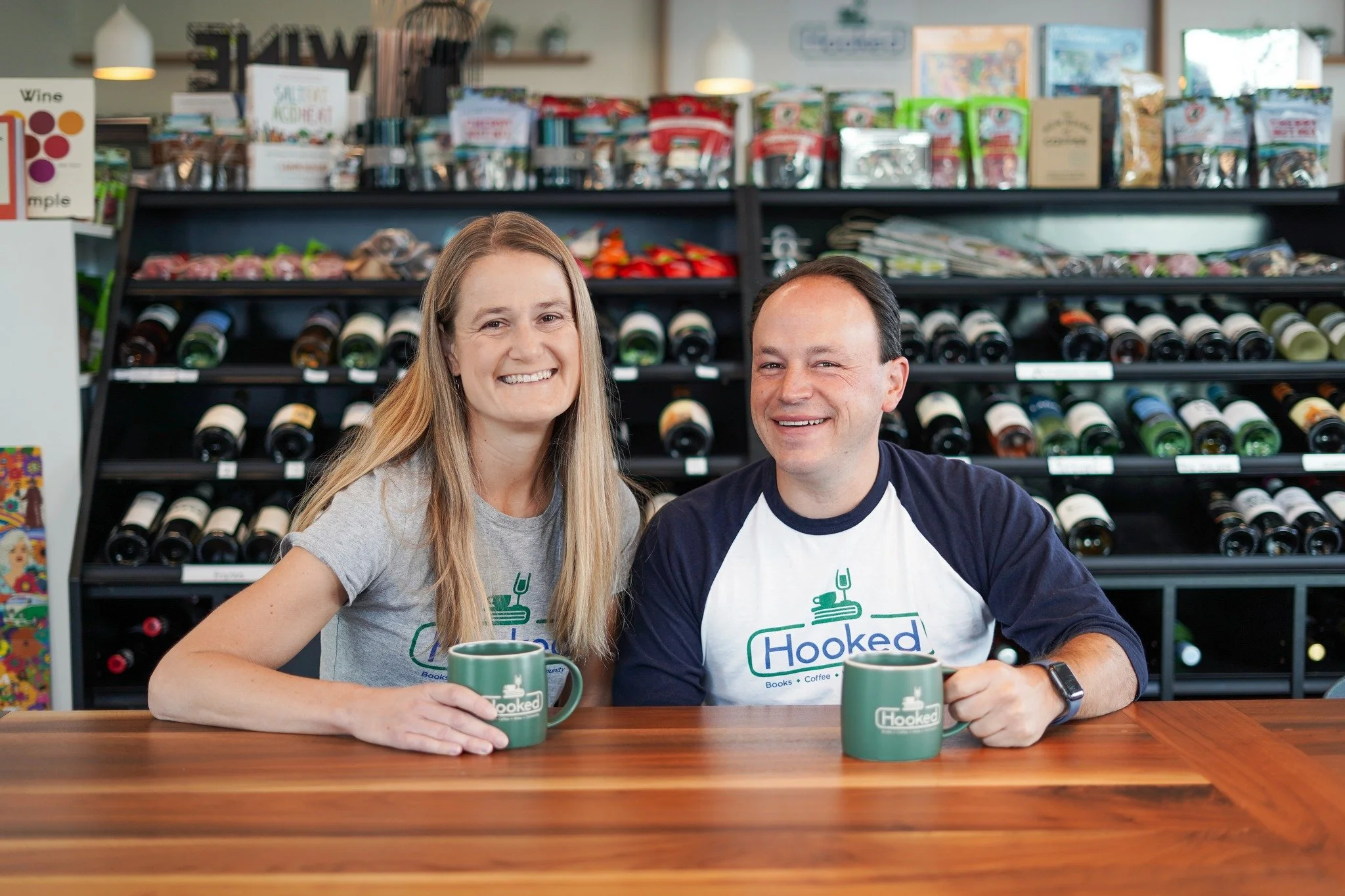 Dr. Sarah Reckhow and Dr. Mark Grossmann sitting at a desk at a cafe, smiling with green coffee mugs in hand.