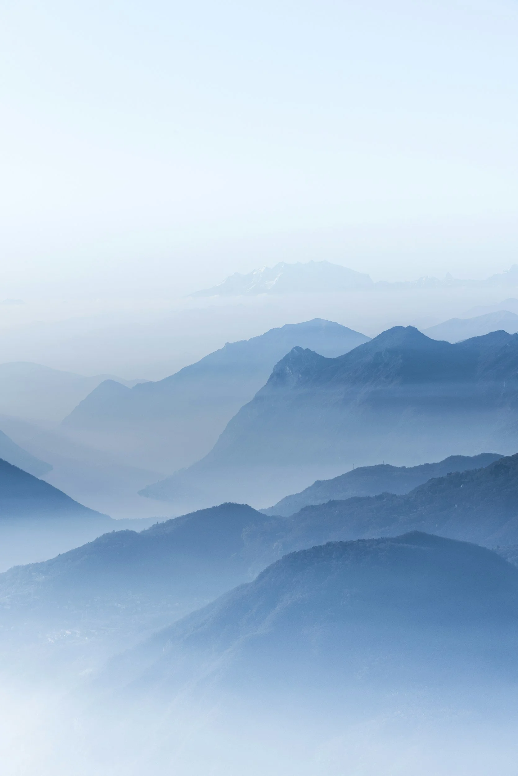 Mountain landscape with multiple layers of mountains shrouded in mist, in shades of blue.