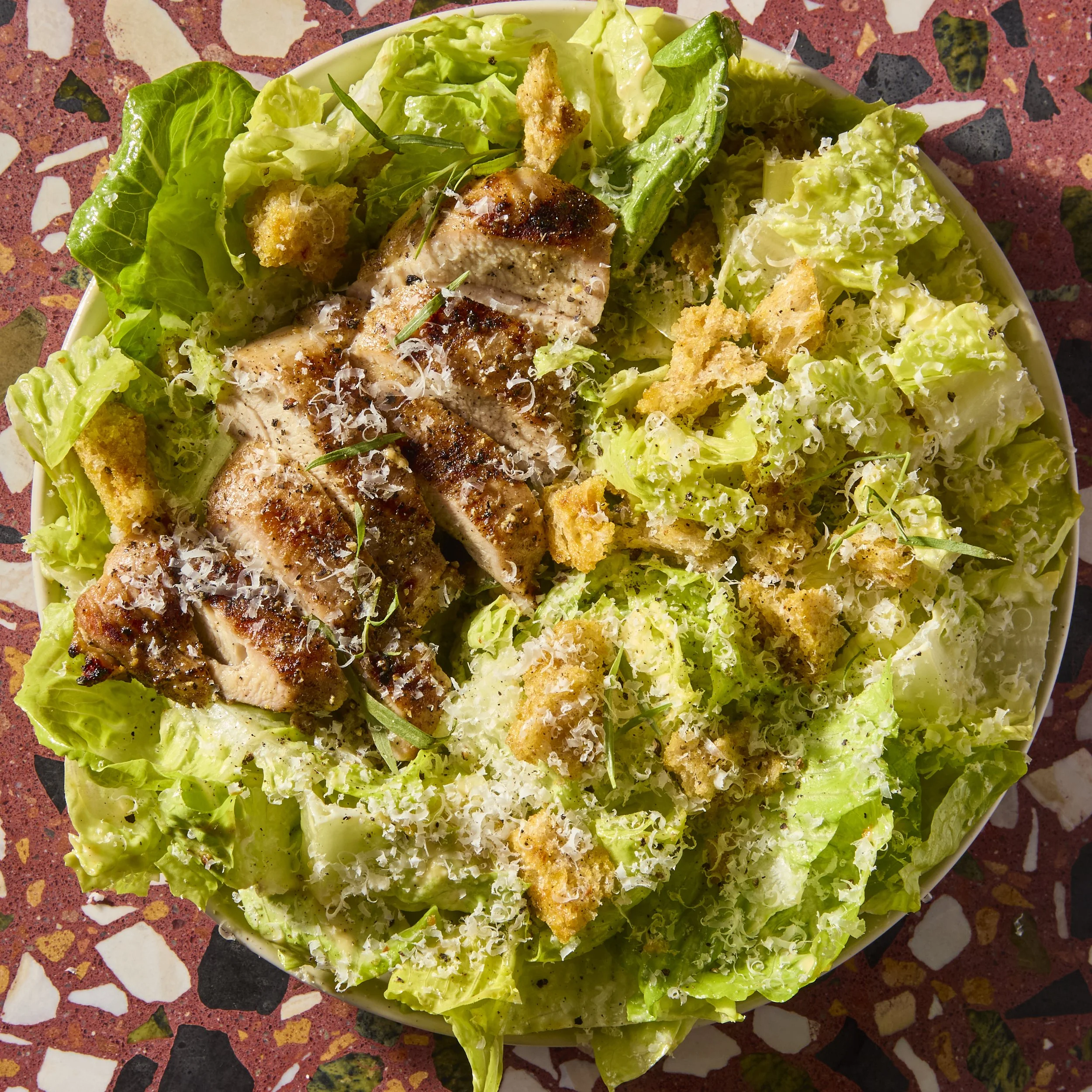 A bowl of fresh green lettuce and crispy fried chicken pieces garnished with grated cheese, served on a vibrant mosaic table surface.