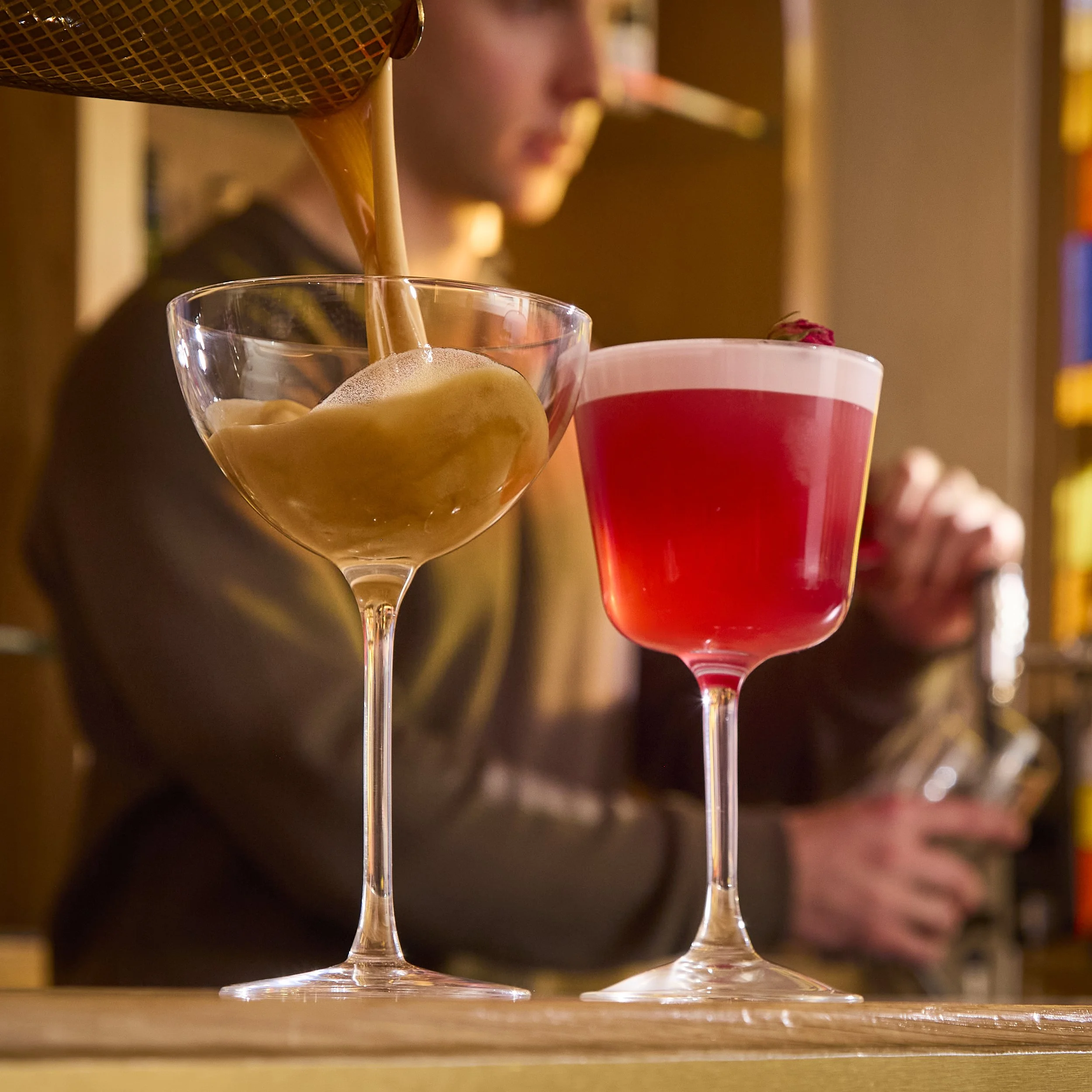 A person pouring a chocolate drink into a glass with a straw on a wooden surface.