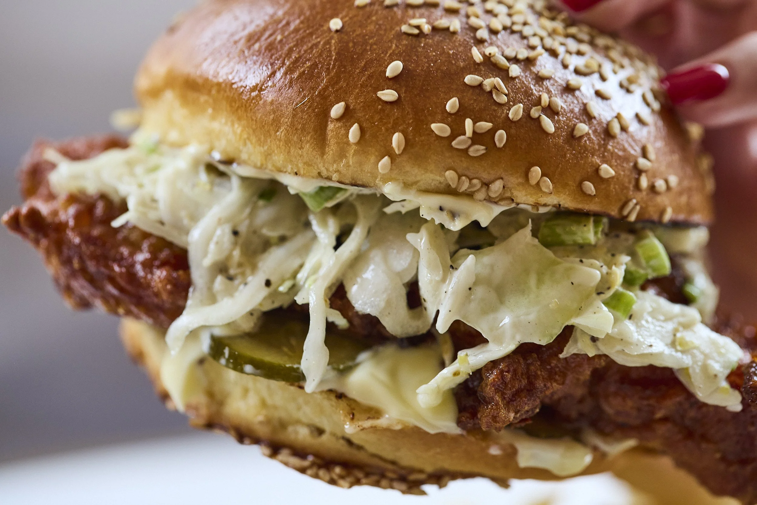 A close-up of a sandwich with a sesame seed bun, shredded lettuce, mayonnaise, and bacon.