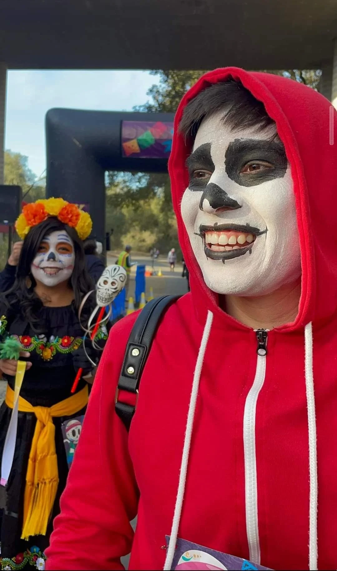People dressed in traditional Mexican Day of the Dead costumes with face paint, including skull designs, at a festive outdoor event.